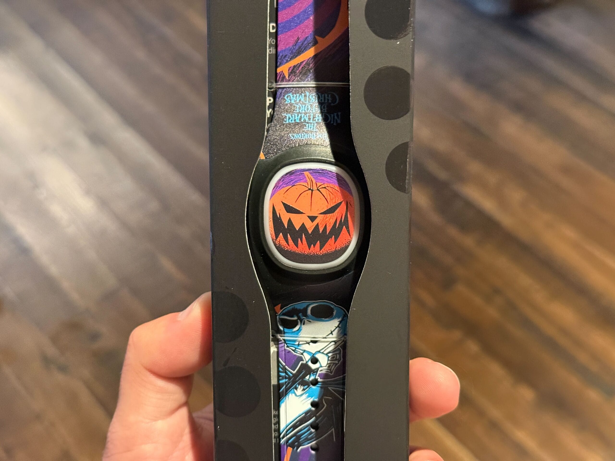 Hand holding a wristband featuring Jack Skellington and Halloween designs inspired by Nightmare Before Christmas in a box.