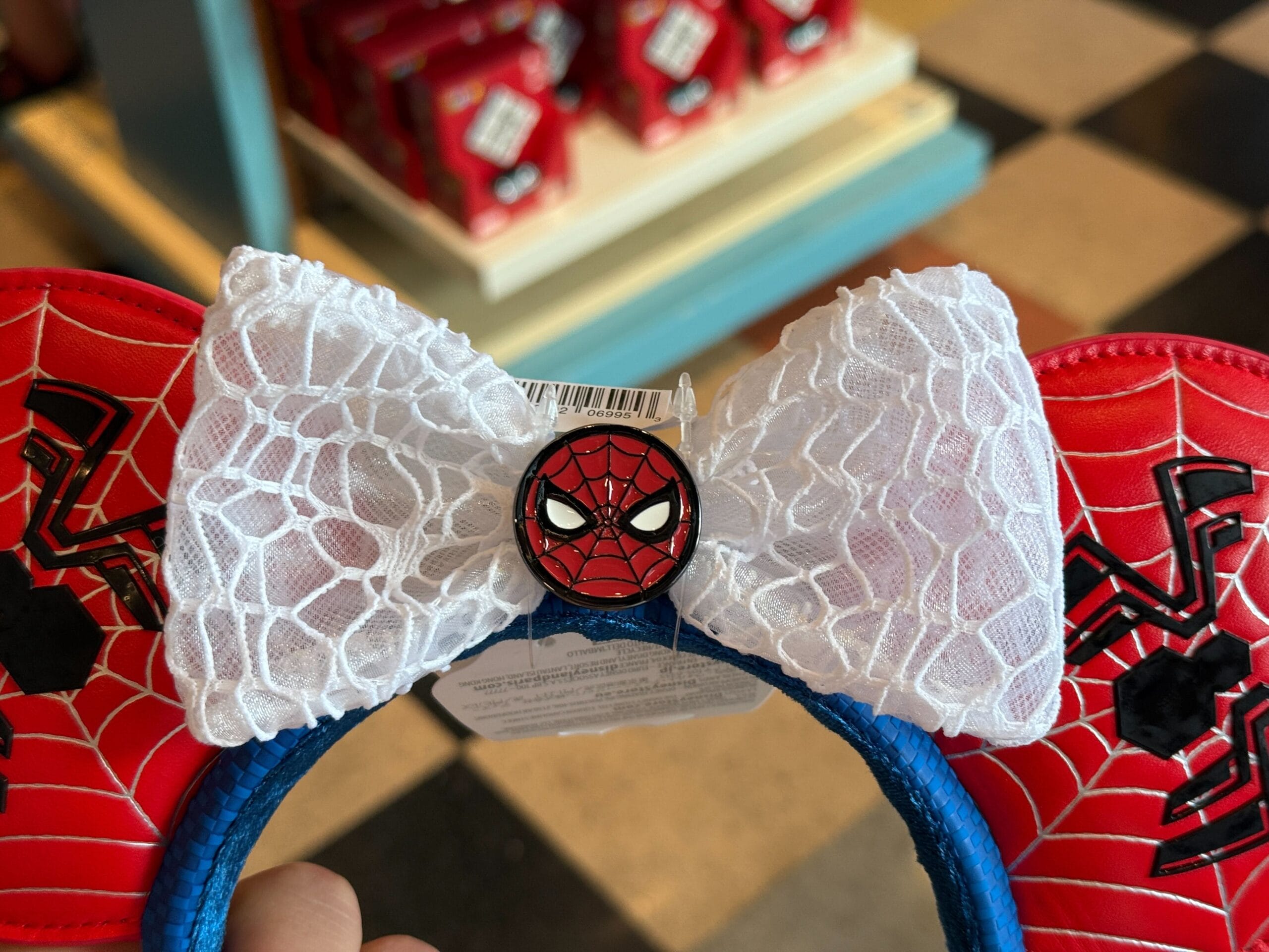 Close-up of Spider-Man-themed Minnie Mouse ears with a white lace bow and Spider-Man face button in the center.
