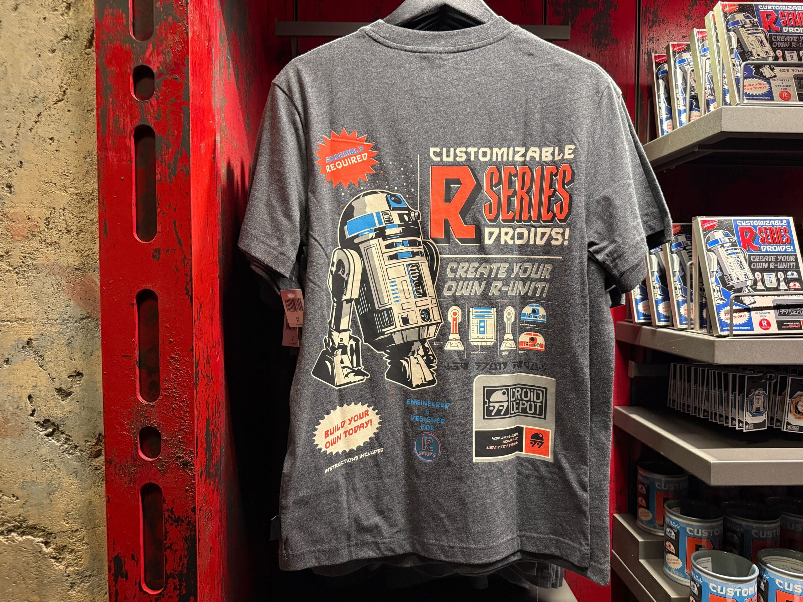 Gray T-shirt featuring a customizable R Series droids design with R2-D2 graphic, displayed in a red store setting.