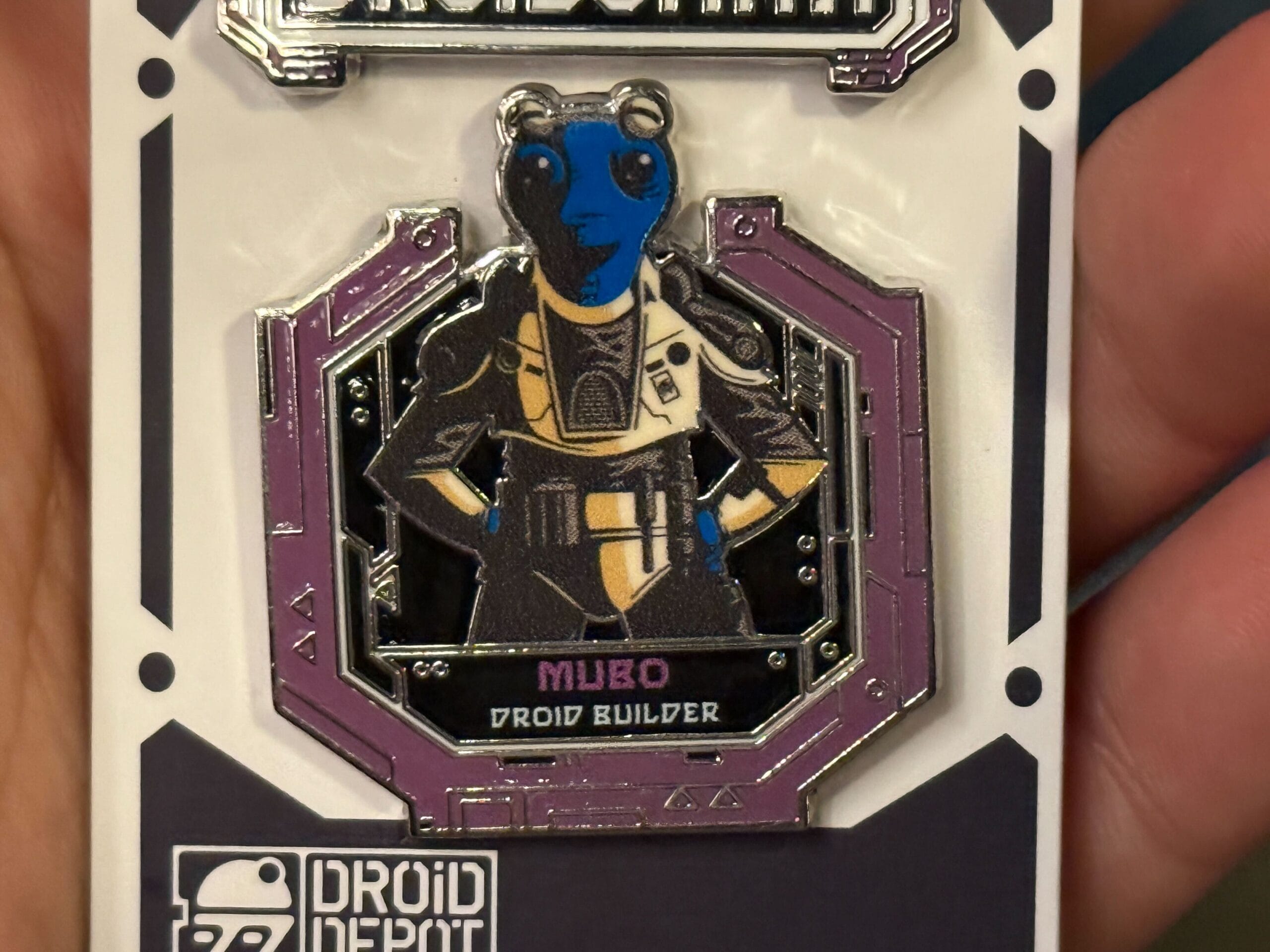 Enamel pin of Mubo, a blue and black alien character, labeled "Droid Builder" from Droid Depot.