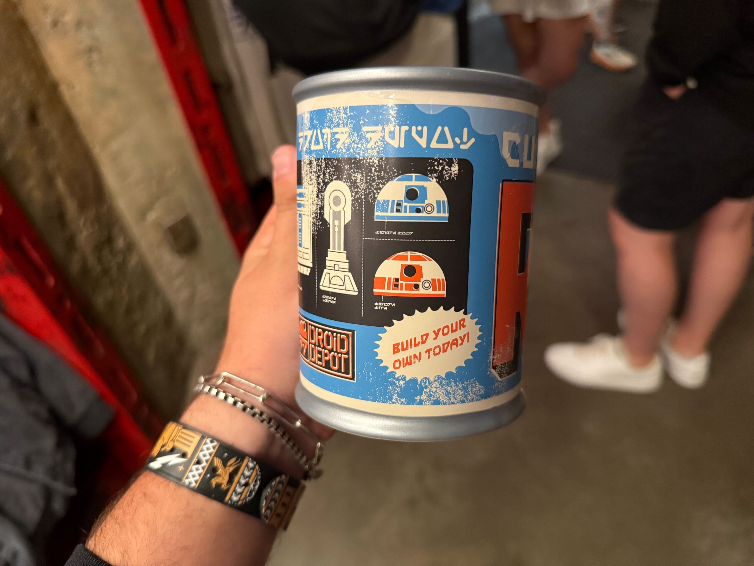 A hand holds a can labeled “Build Your Own Droid” featuring Star Wars droids and design instructions.