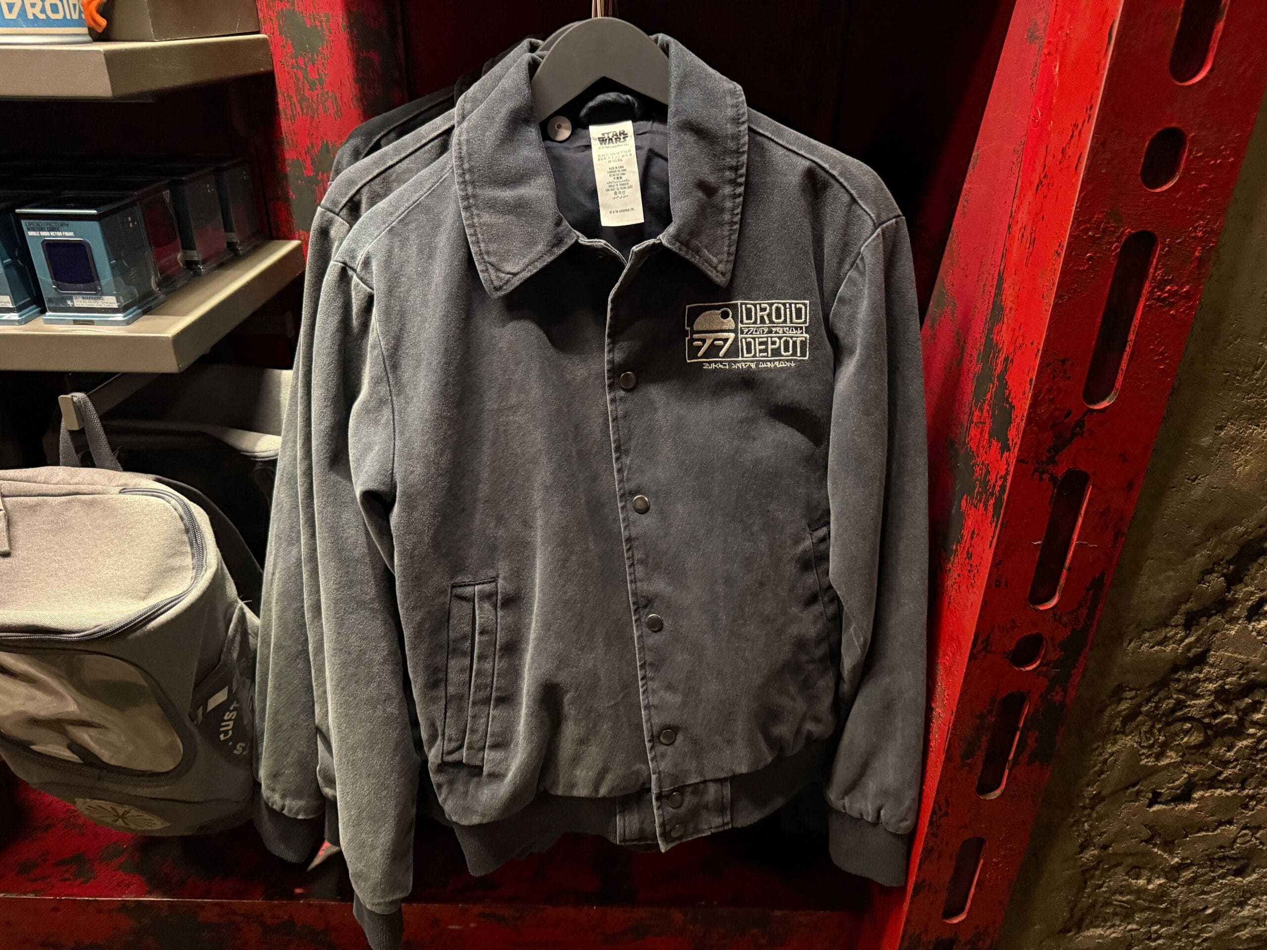 A gray “Droid Depot” jacket hangs on a rack, displayed in a store with red shelves.