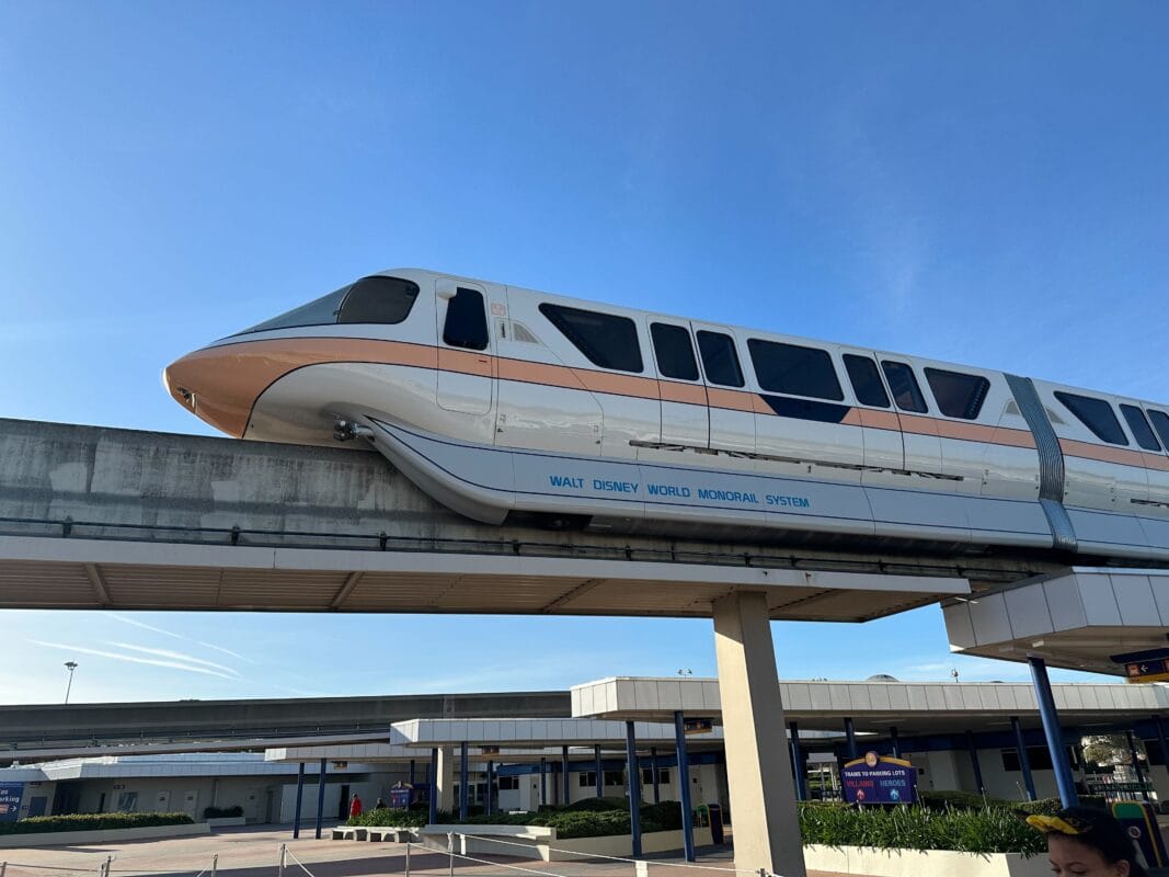 A Disney Transportation and Ticket Center monorail glides on an elevated track at Walt Disney World on a clear, sunny day.