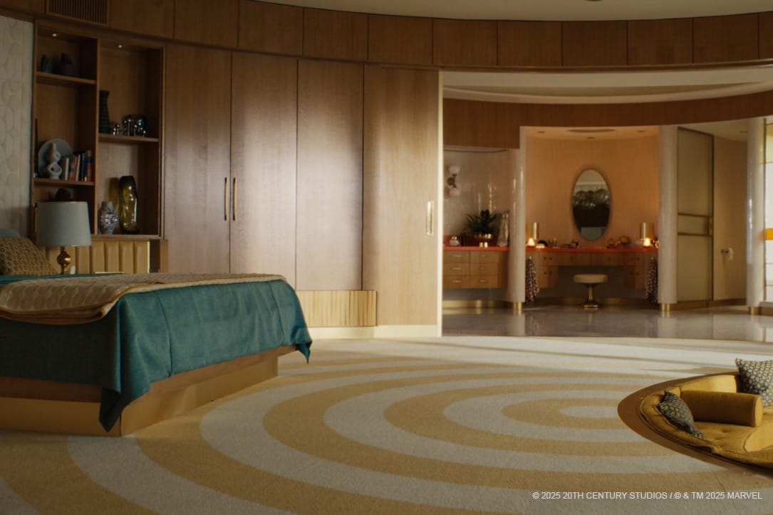 Spacious, mid-century bedroom with a circular yellow-and-white rug, wood paneling, and an open doorway to a lit vanity area.