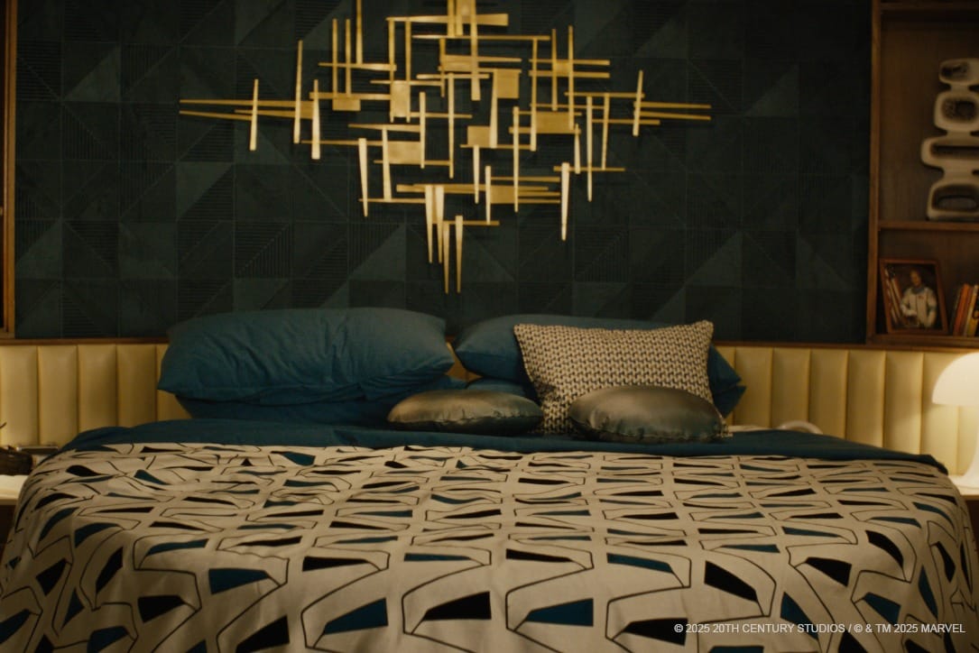 A mid-century bed with dark green and gold bedding, geometric pillows, and a gold abstract wall sculpture above the headboard.