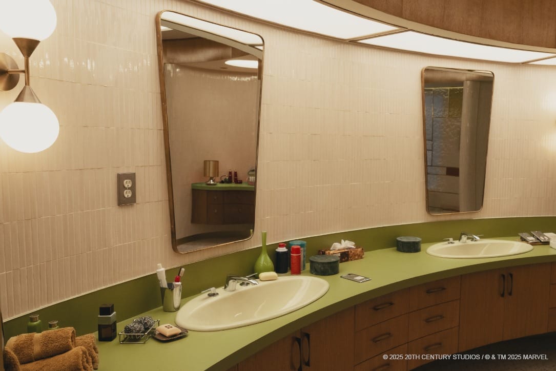 Double bathroom sink with green countertop, large mirrors, and various toiletries neatly arranged.