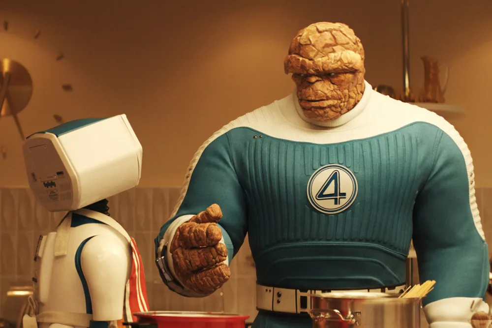 A large, rock-skinned Fantastic Four hero in blue greets a small robot in a kitchen after a big box office opening weekend.