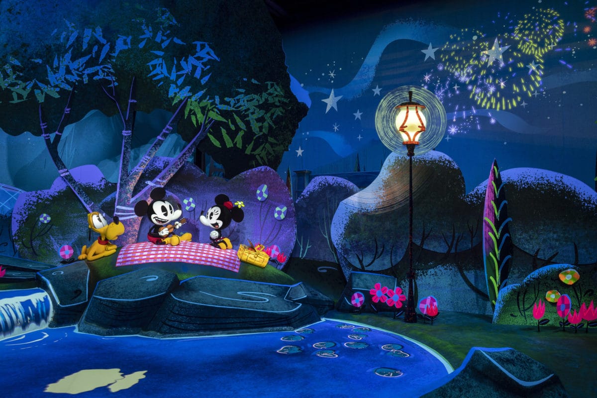 Mickey and Minnie picnic by a stream under fireworks, a magical night inspired by Walt Disney World history.