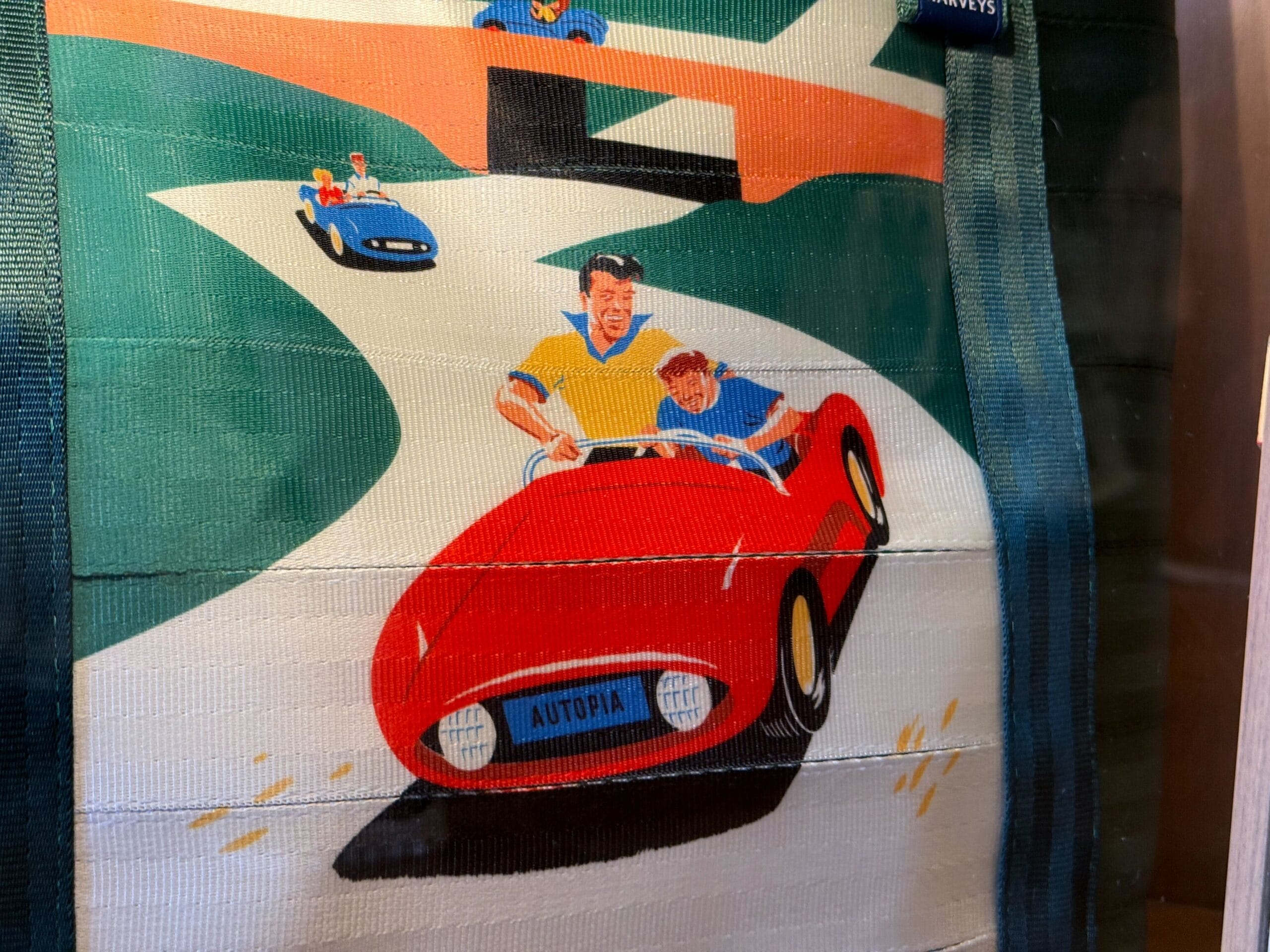 Illustration of a man and child driving a red Autopia car on a winding road, with more cars in the background.