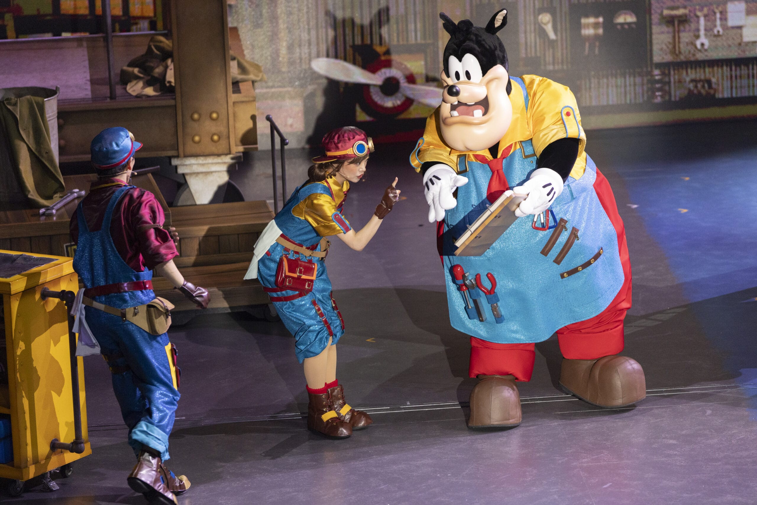 Three performers, including Pete, bring dreams take flight on stage in colorful engineer outfits at Tokyo DisneySea.