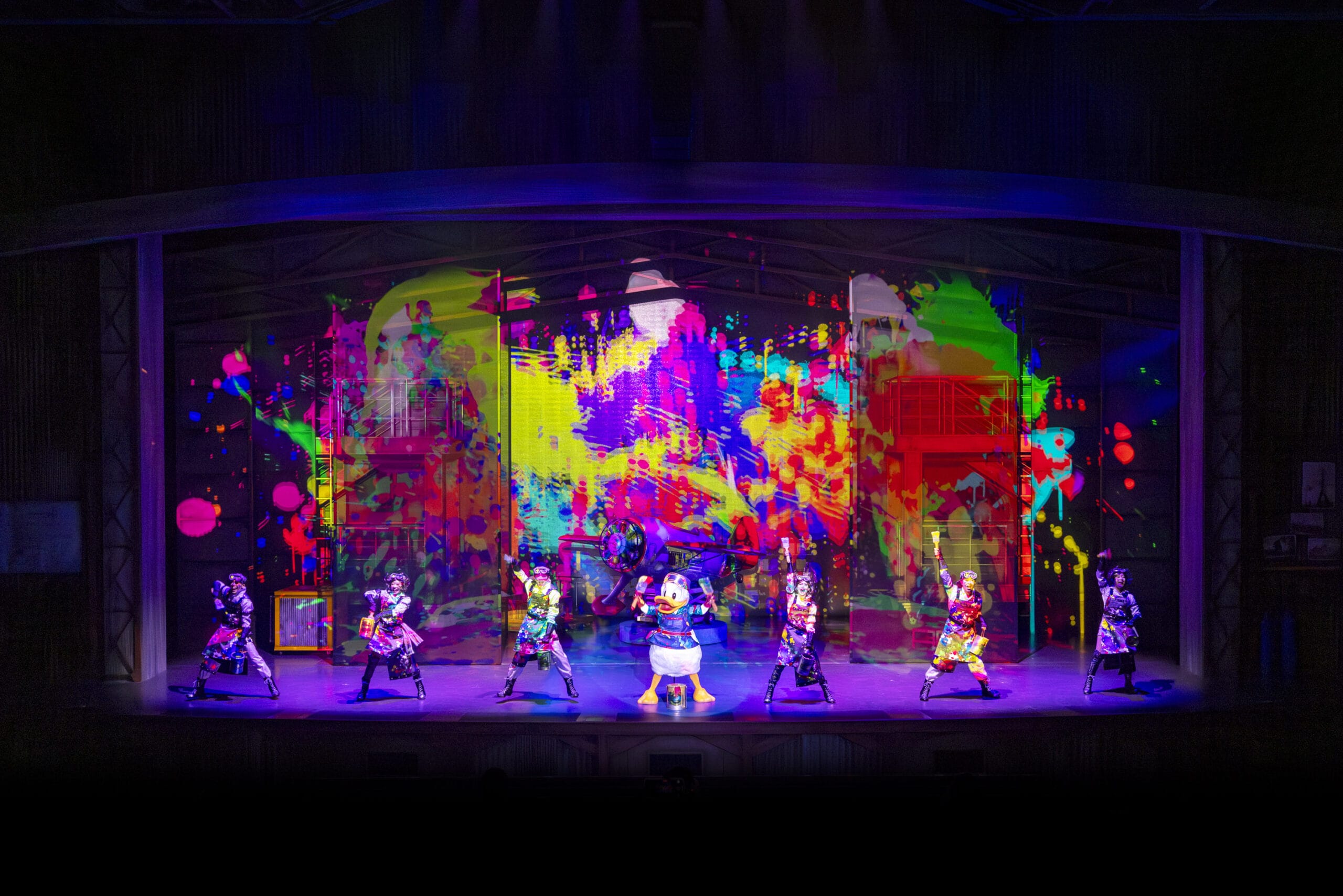 Performers in colorful costumes dance onstage at Tokyo DisneySea as dreams take flight with vibrant, abstract projections.