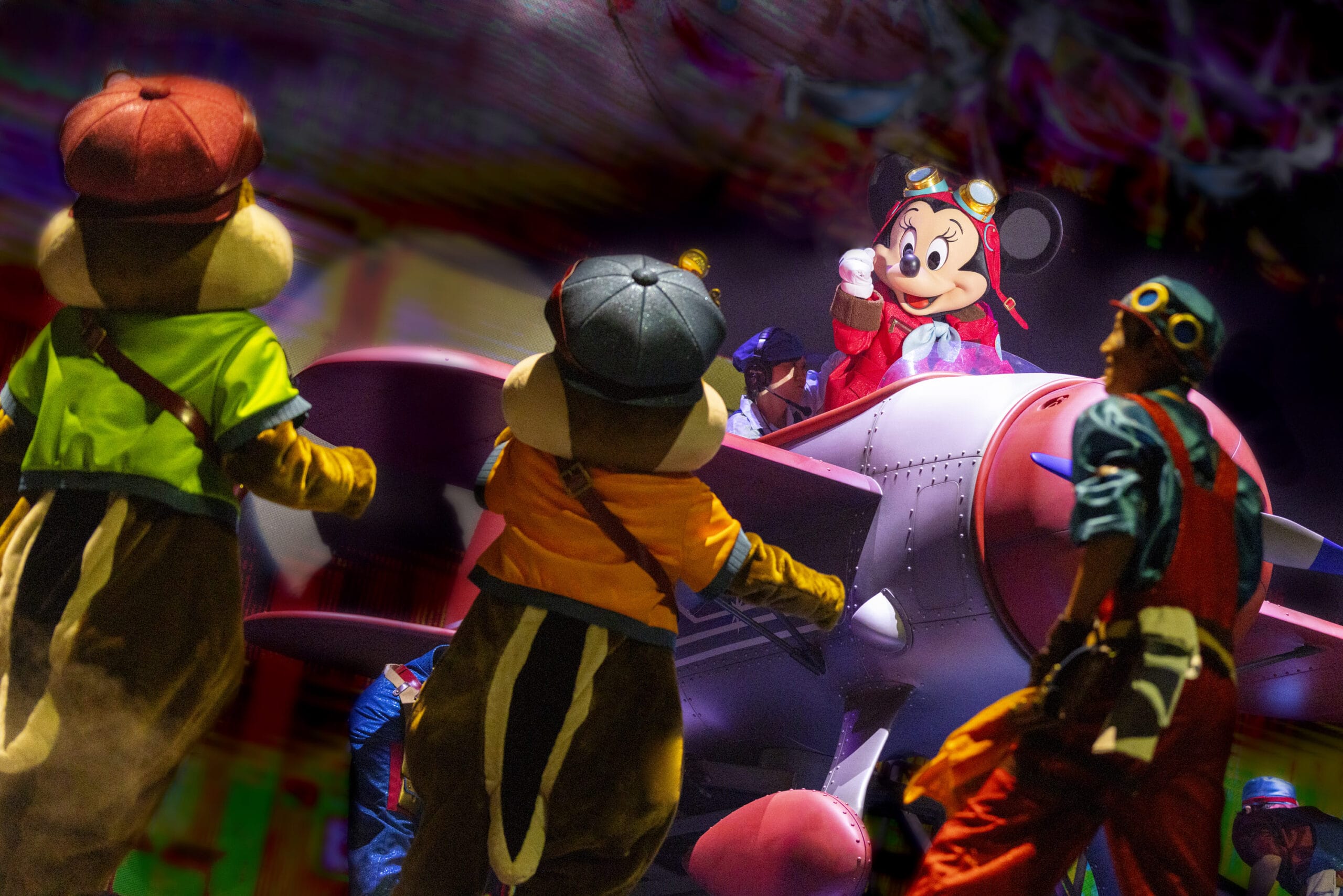 Mickey Mouse in aviator gear sits on a plane at Tokyo DisneySea, where dreams take flight with colorful performers on stage.