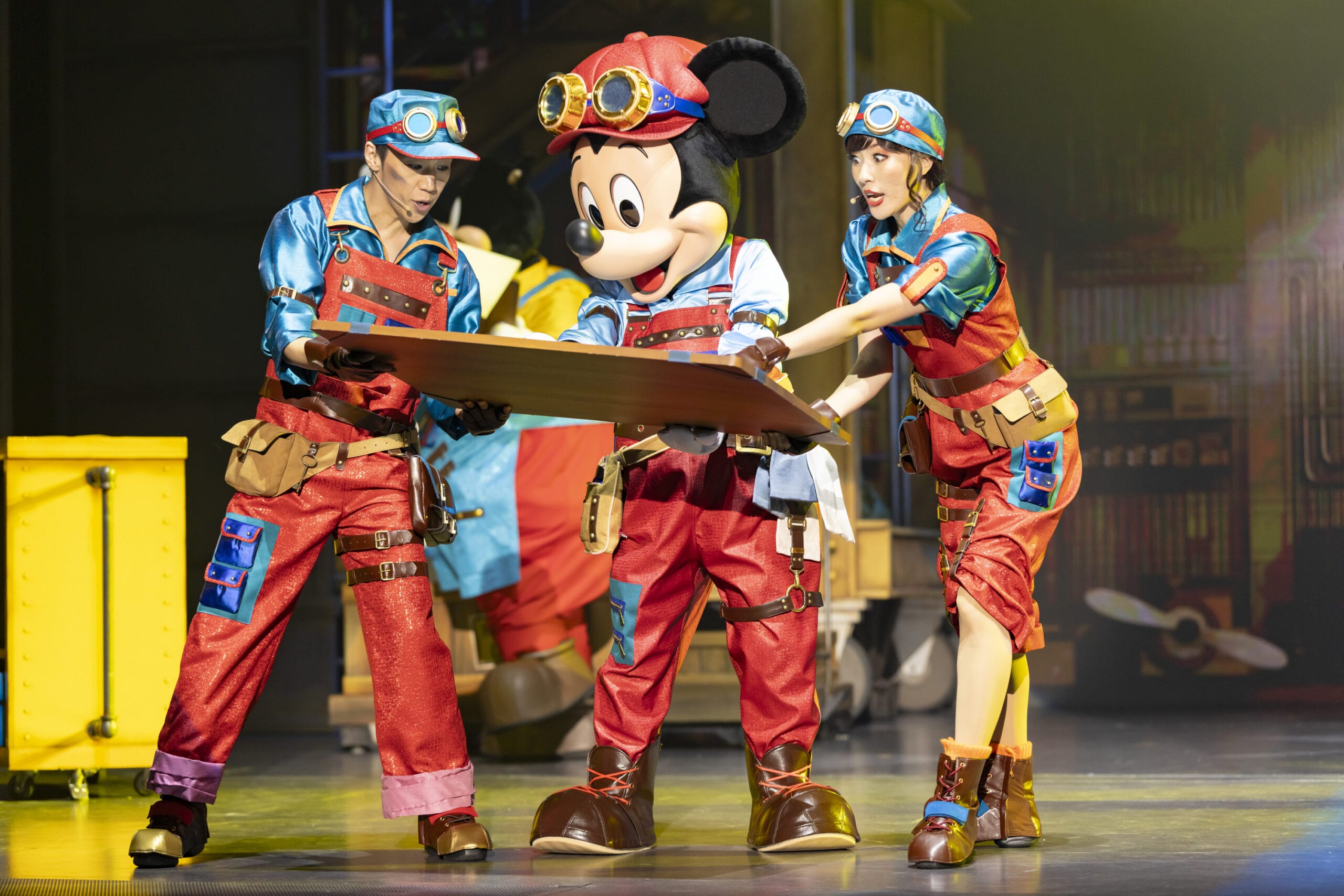 Three performers in colorful uniforms, with Mickey Mouse, examine a plank onstage at Tokyo DisneySea where dreams take flight.