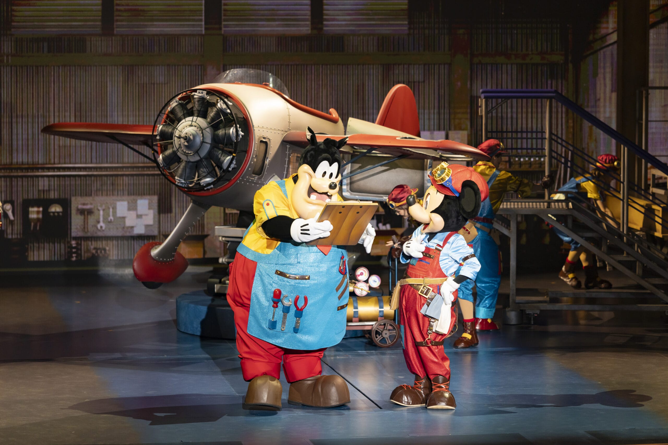 Mickey Mouse and Pete, dressed as mechanics, talk by a red airplane at Tokyo DisneySea as dreams take flight on stage.