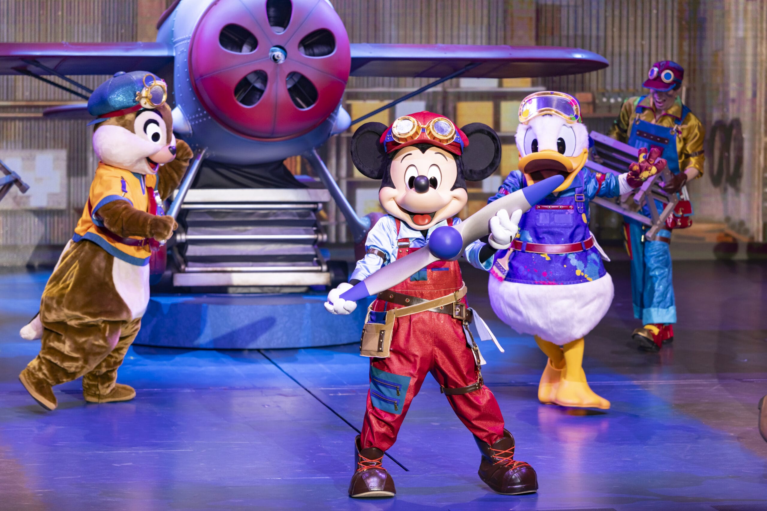 Mickey, Donald, and Chip in pilot costumes take the stage at Tokyo DisneySea as dreams take flight before a colorful airplane.