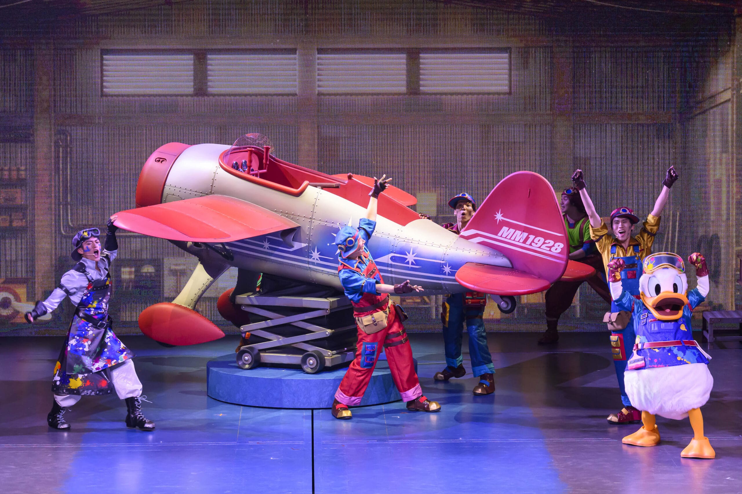 Performers in colorful costumes and Donald Duck pose beside a toy airplane at Tokyo DisneySea, where dreams take flight.