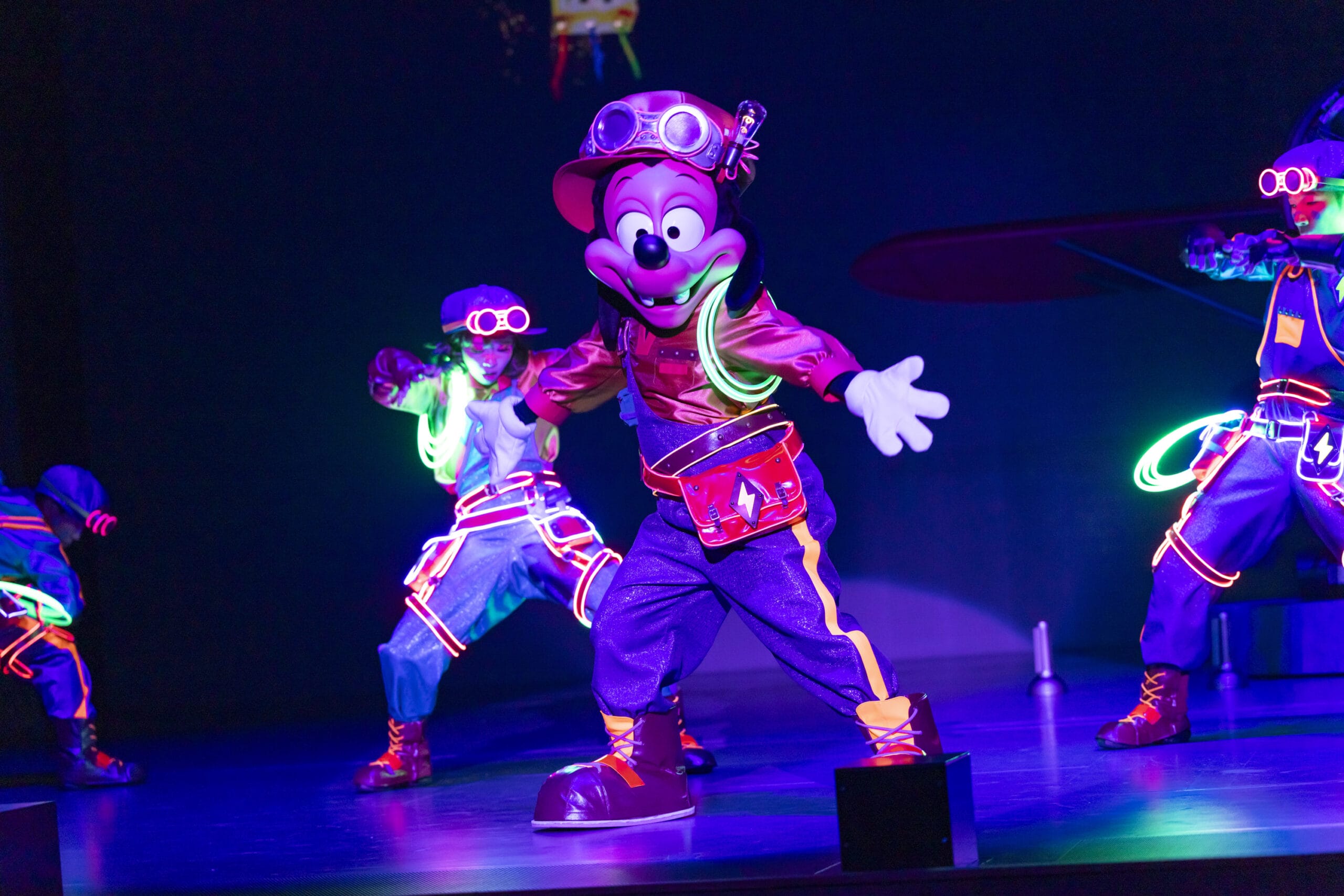 A performer in a neon Mickey Mouse costume dances as dreams take flight on stage with glowing outfits at Tokyo DisneySea.