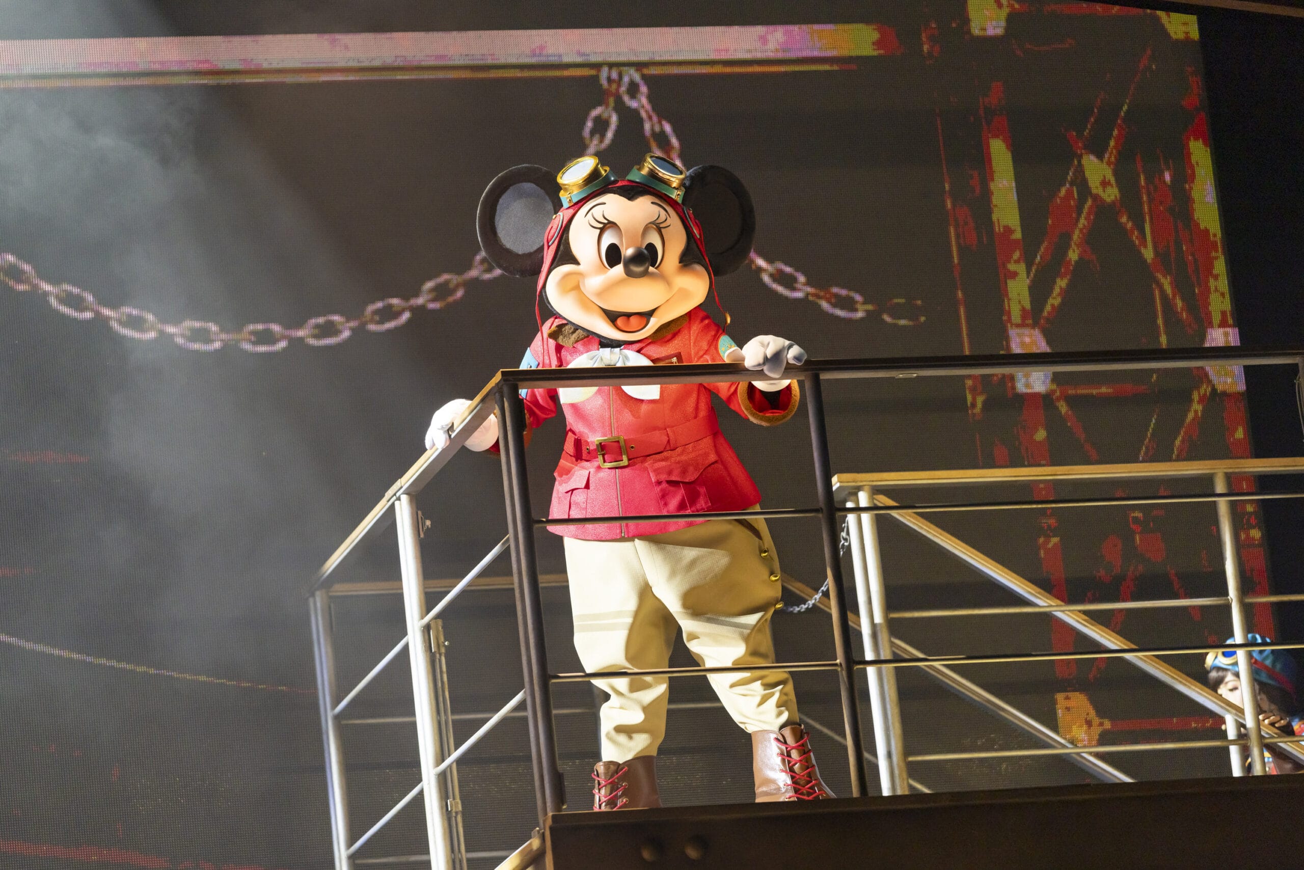 Minnie Mouse in a red jacket stands on a metal stage at Tokyo DisneySea, where dreams take flight under bright stage lights.