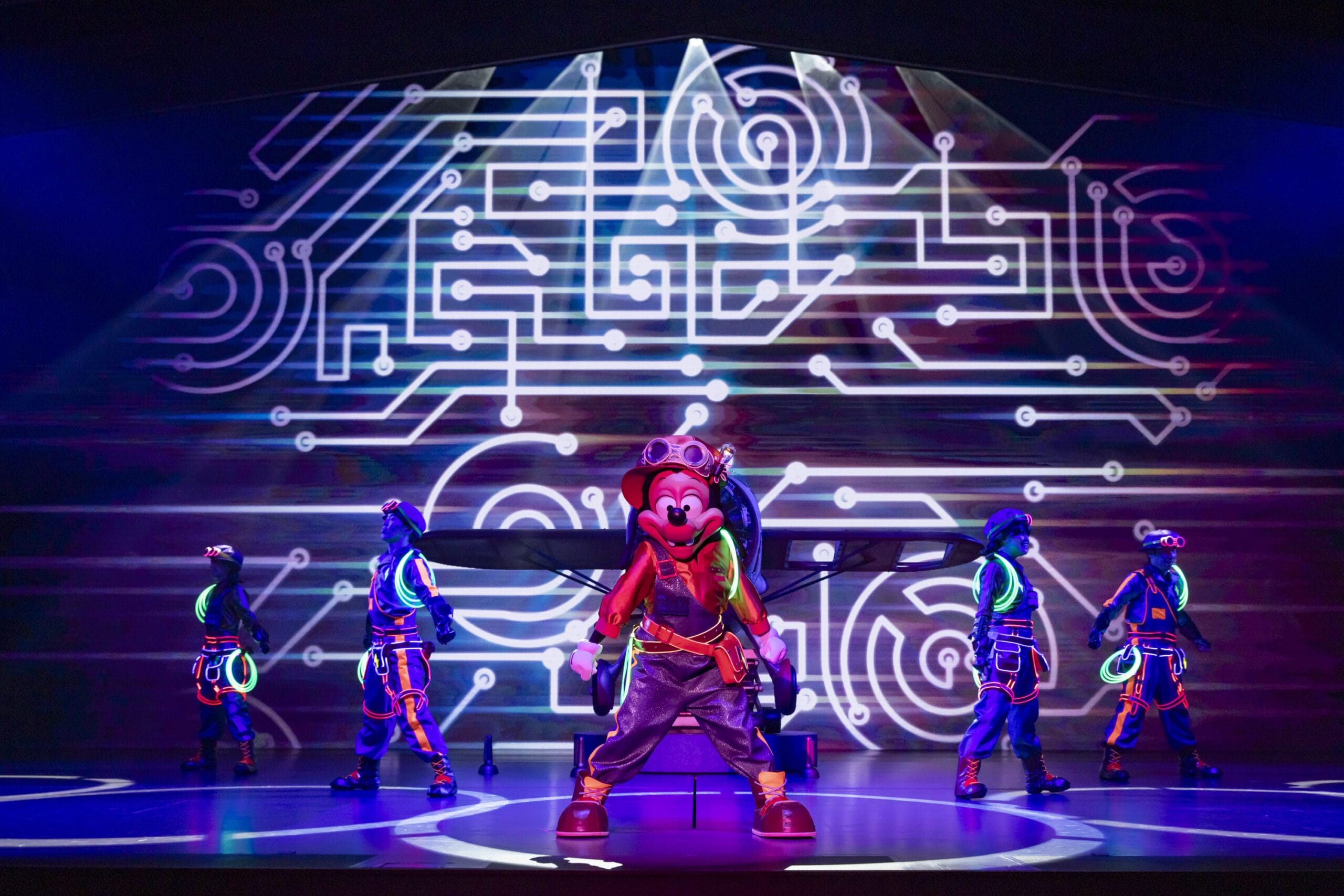A performer in red dances on stage at Tokyo DisneySea, where neon-clad dancers and dreams take flight amid a digital backdrop.