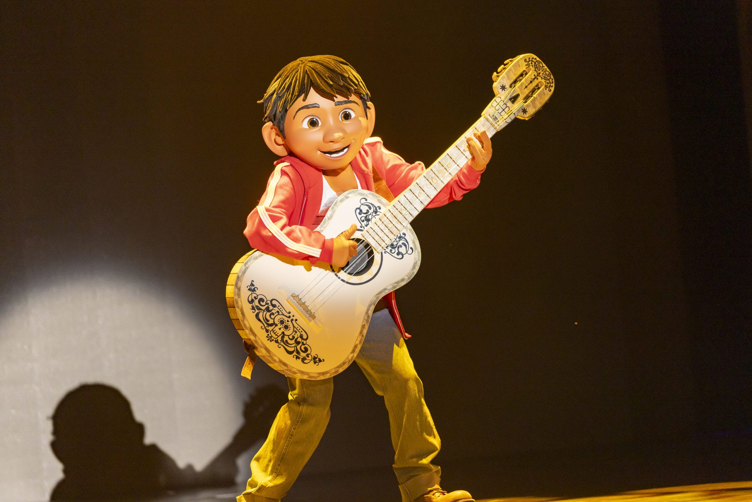 A child in a red jacket and jeans plays a white guitar on stage at Tokyo DisneySea, where dreams take flight.