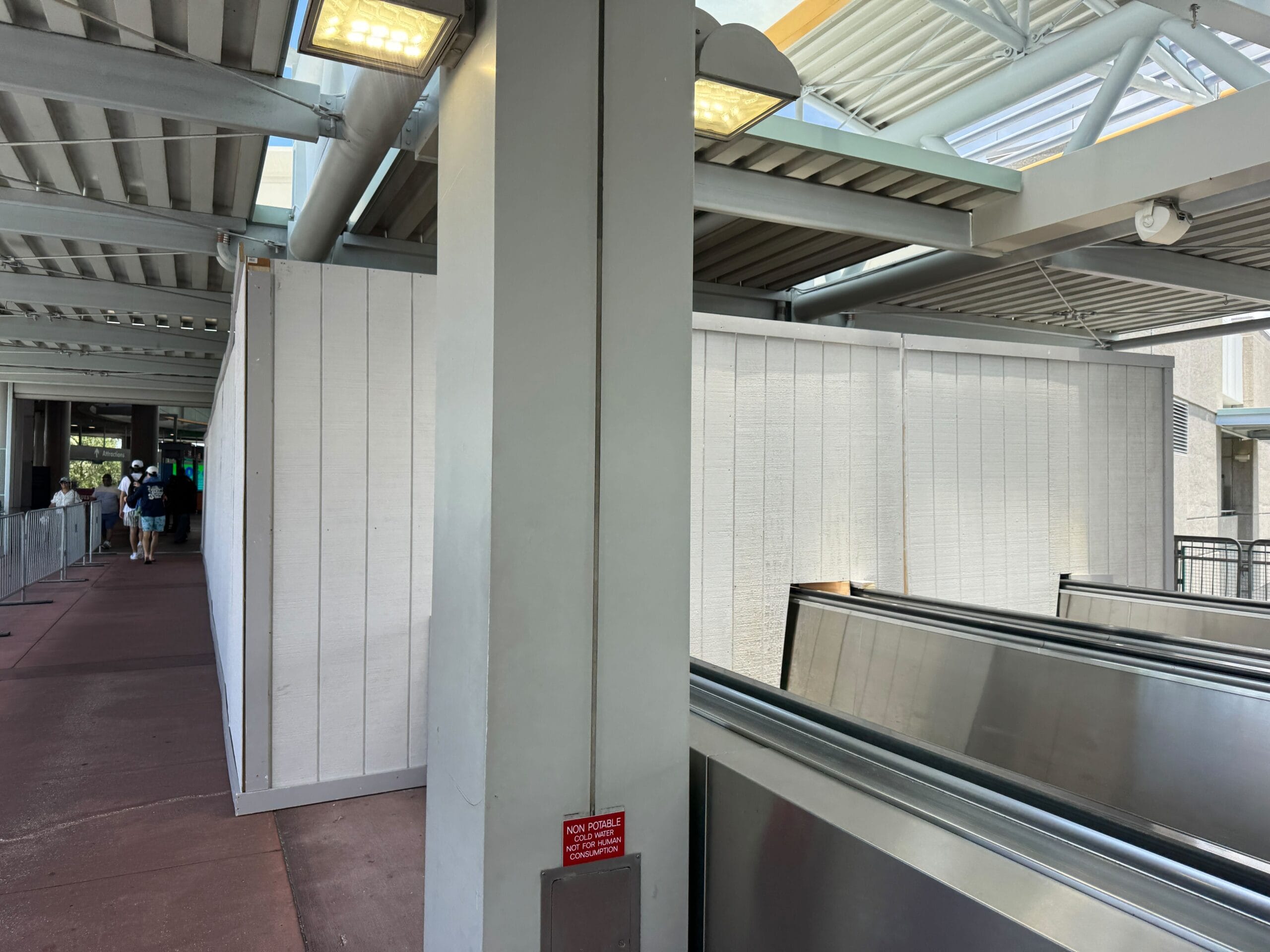 Construction walls blocking part of a moving walkway under a covered outdoor area in Universal Orlando Resort.