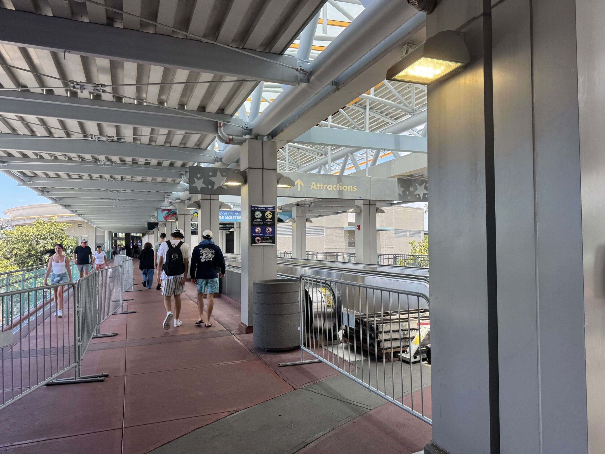 People walking along a covered walkway with a sign overhead pointing toward "Attractions" in Universal Orlando Resort.