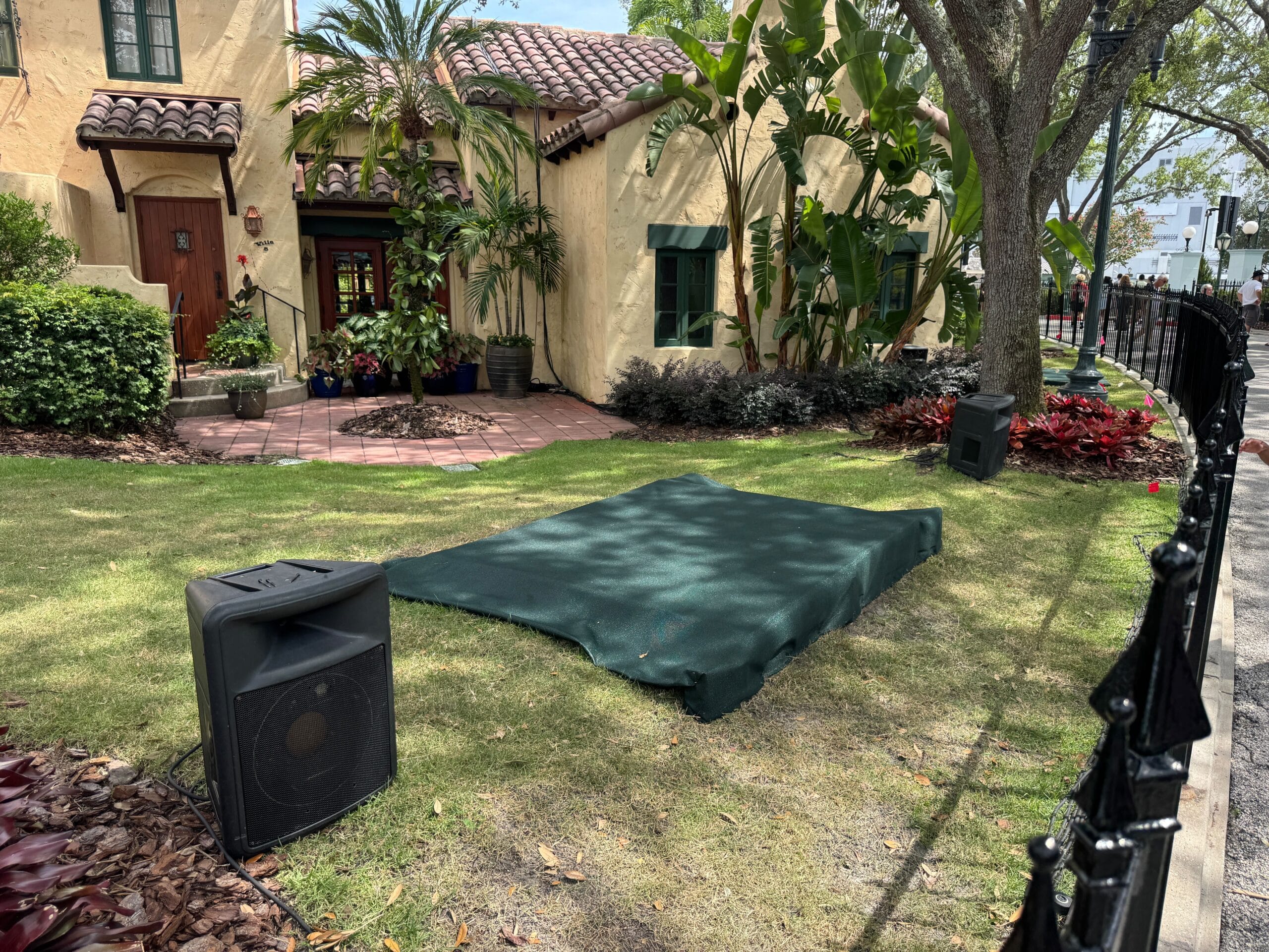 A green tarp covers grass near a sidewalk, as Prep begins for a Scare Zone outside a tan stucco house.
