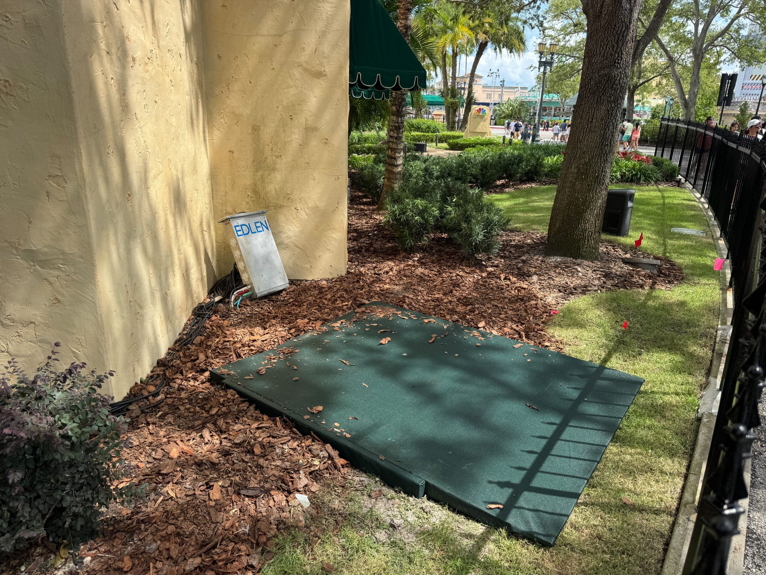A green mat preps the ground for a Scare Zone near a building with an "EDLEW" sign, surrounded by mulch and trees.
