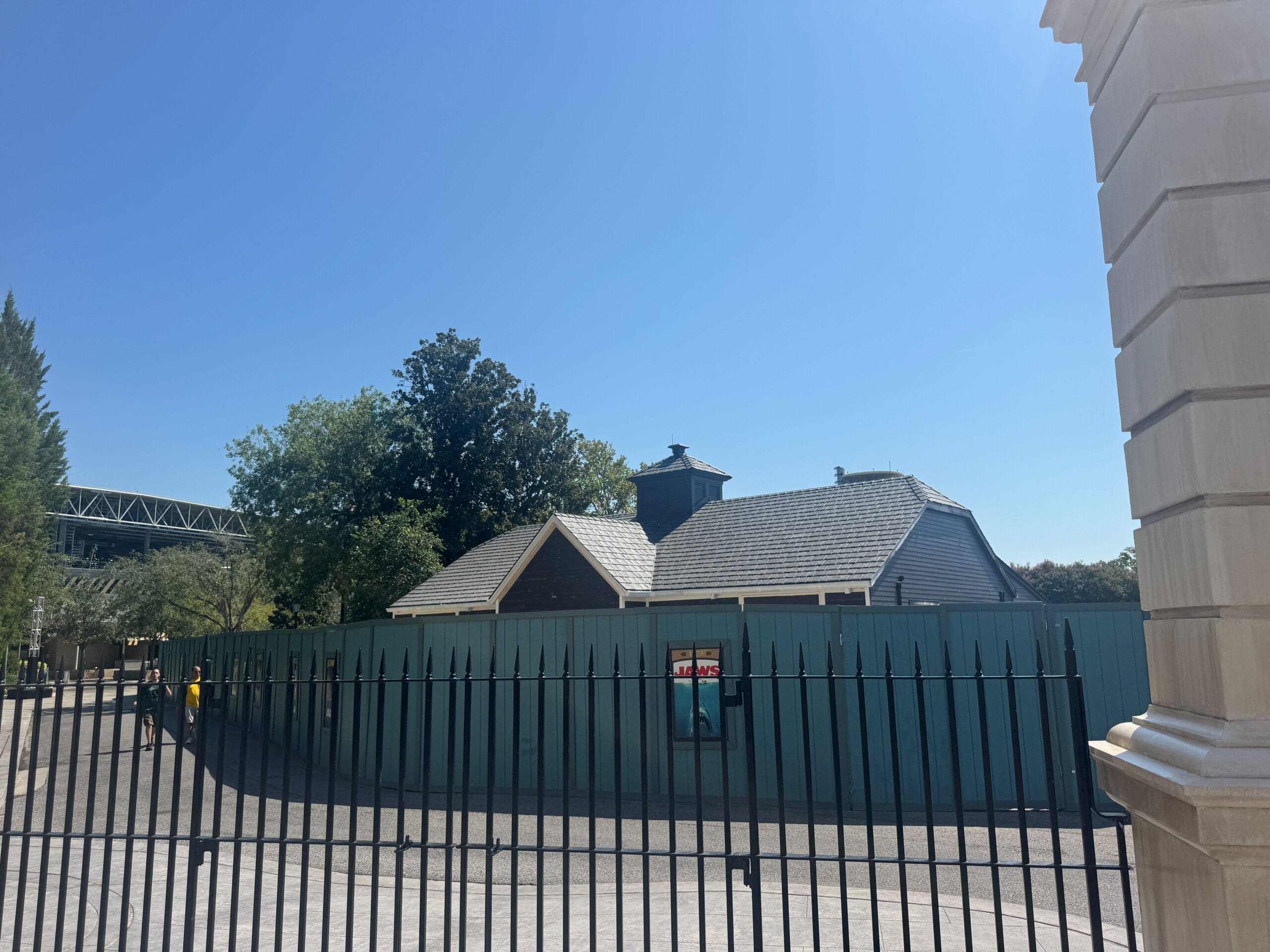 A fenced-off building under construction with a blue sky and trees in the background.