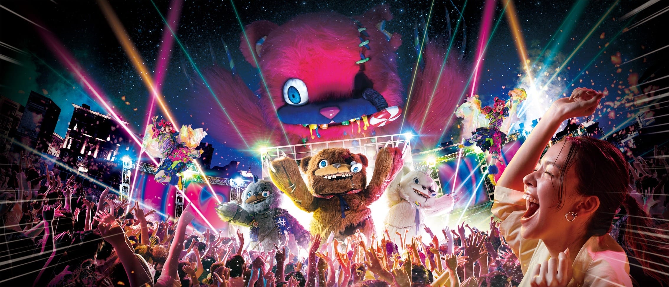 Colorful crowd at a concert featuring HamiKuma Candy mascots, lasers, confetti, and a woman cheering in the foreground.