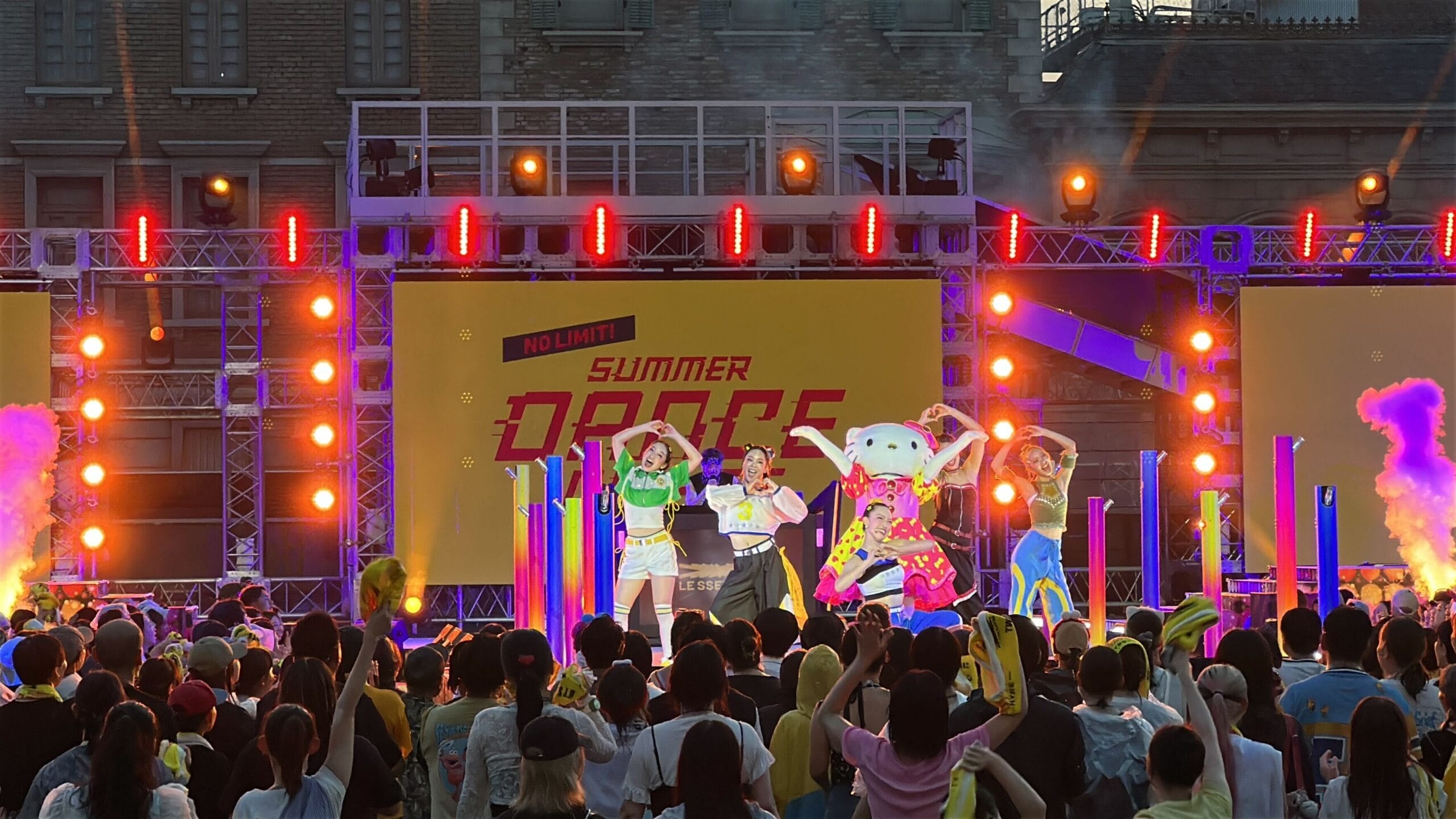 Performers dance on a brightly lit stage labeled “Summer Dance Nights” as a crowd enjoys the sunset—perfect for photos.
