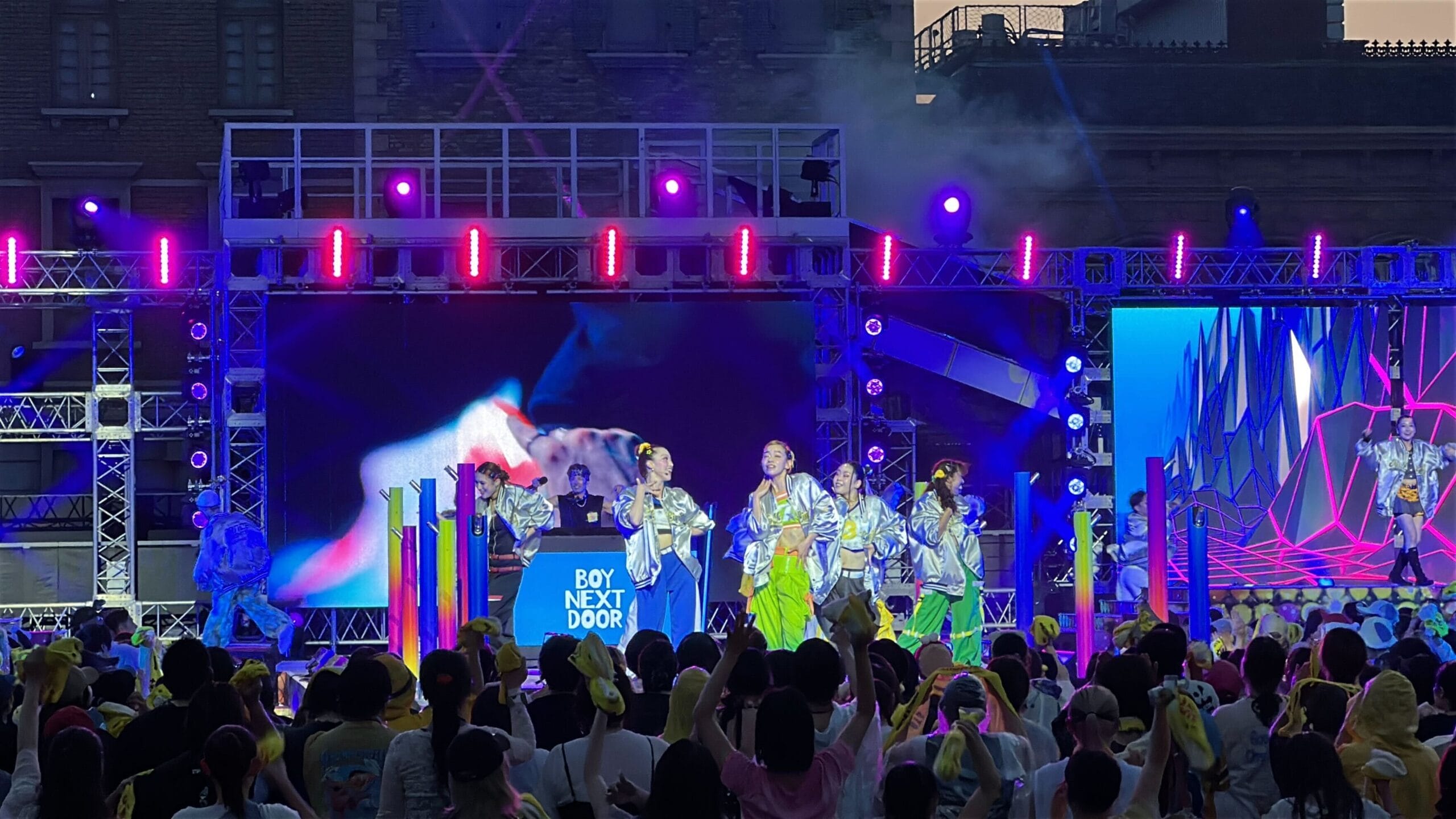 A pop group lights up the stage at Summer Dance Nights, thrilling a cheering crowd under the night sky.