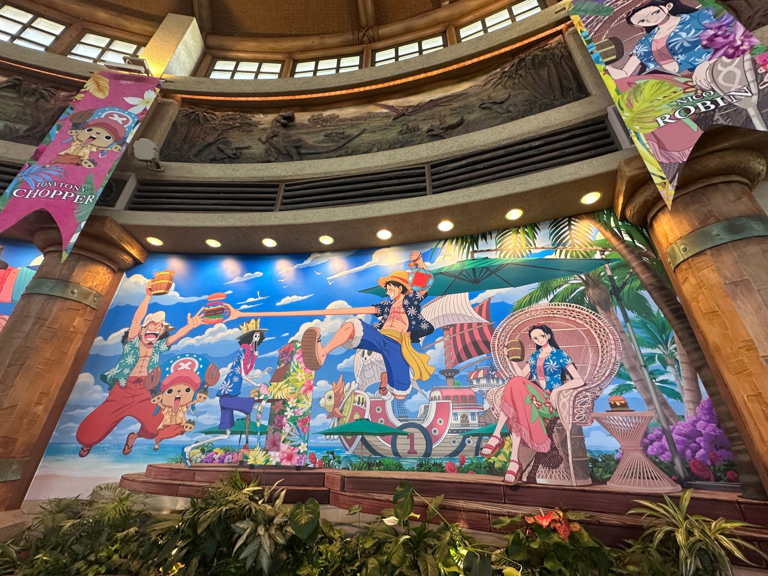 Colorful mural of anime characters in summer outfits with a tropical, beach, and ocean background inside a large building.