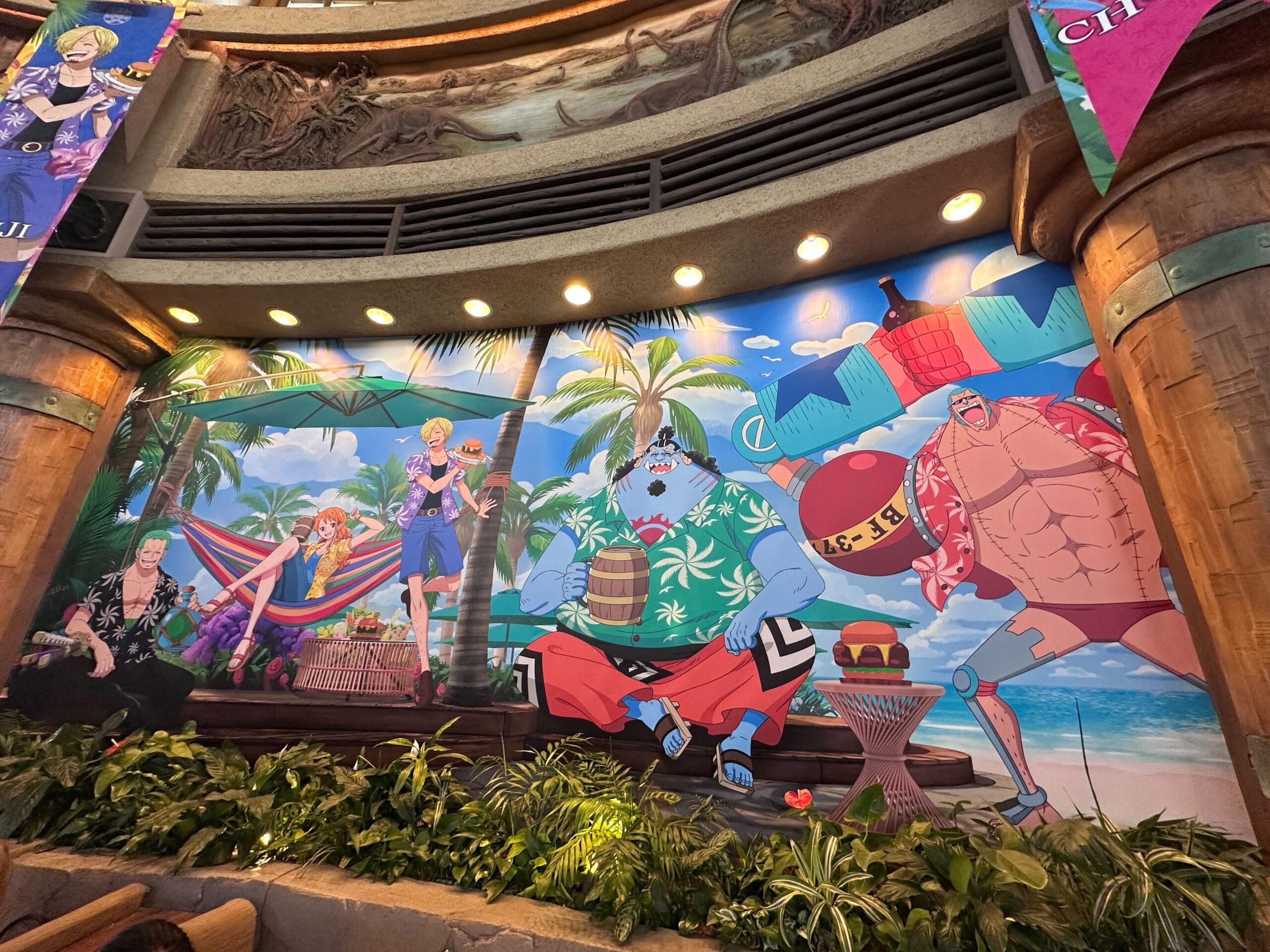 Colorful mural of animated characters relaxing on a tropical beach with palm trees, drinks, and ocean in the background.