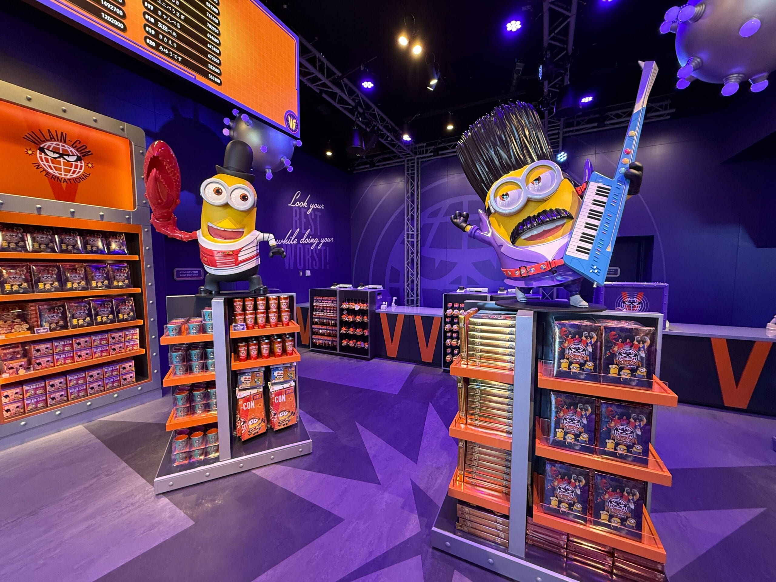 Store with large Minion statues, one holding a paddle, the other with a keyboard, surrounded by colorful merchandise displays.