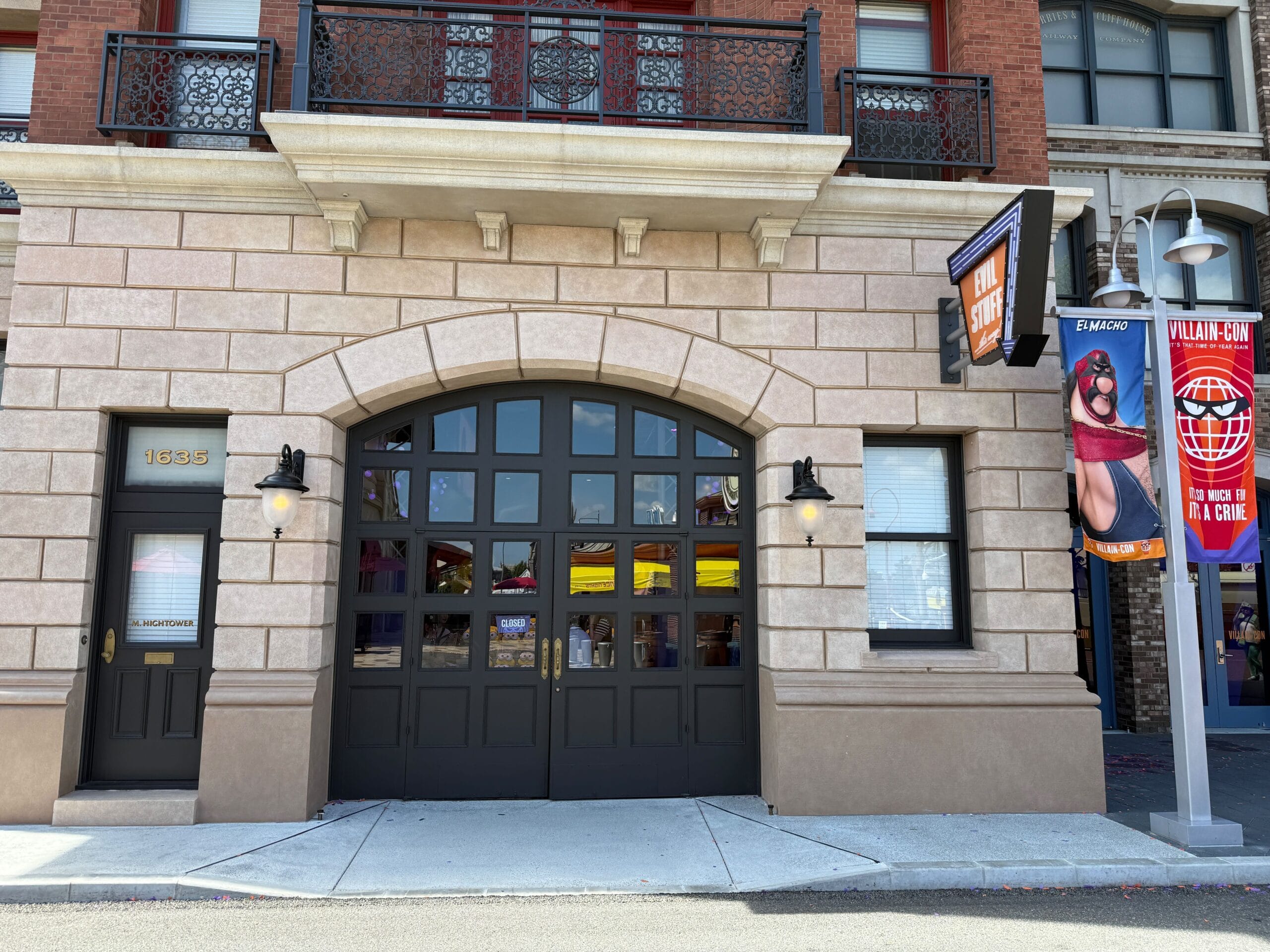 Building with large black double doors, tan stone facade, and a Villain-Con banner hanging on the right side.
