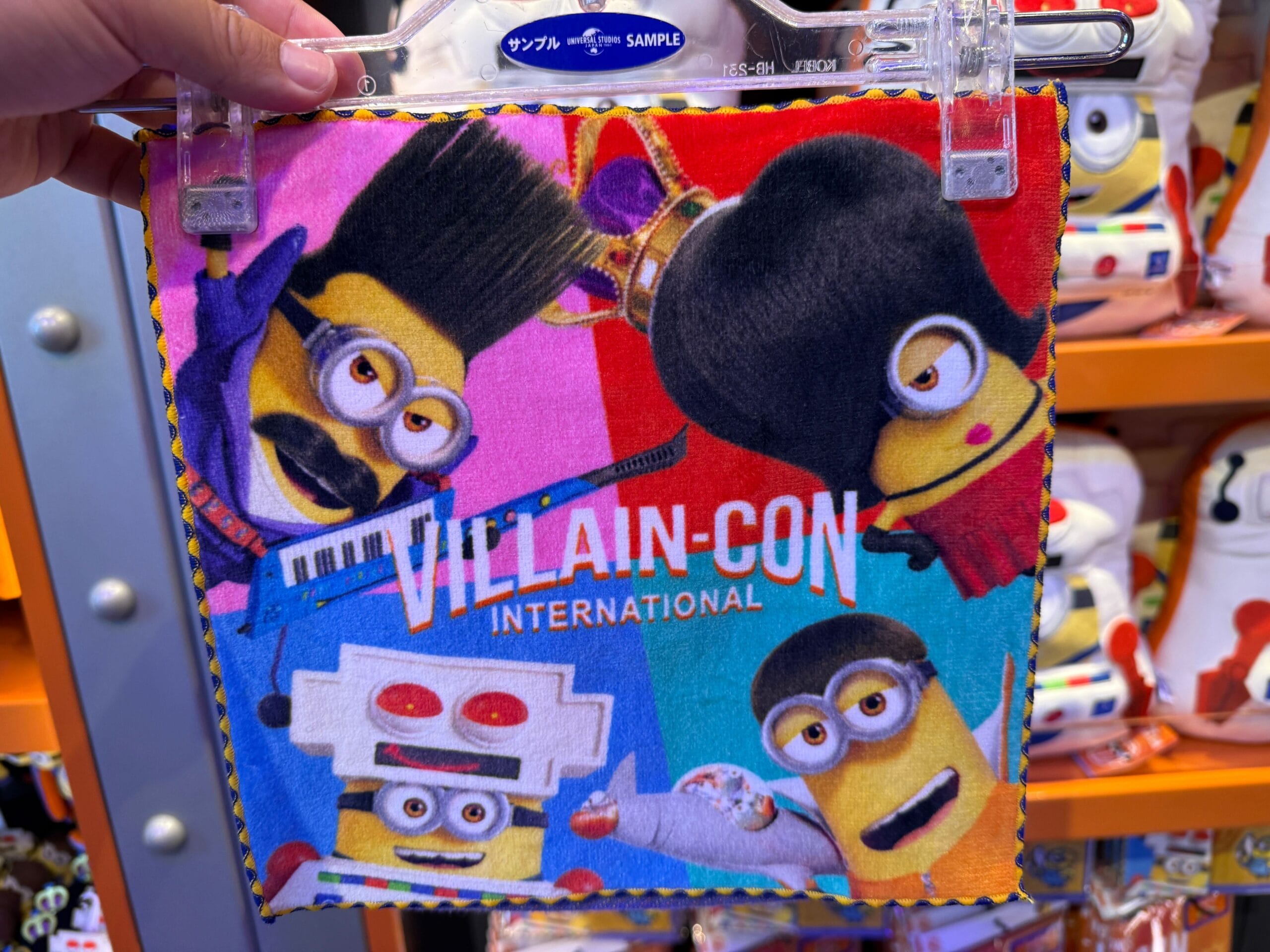 A colorful hand towel features four Minions in costumes with "VILLAIN-CON INTERNATIONAL" printed across the front.