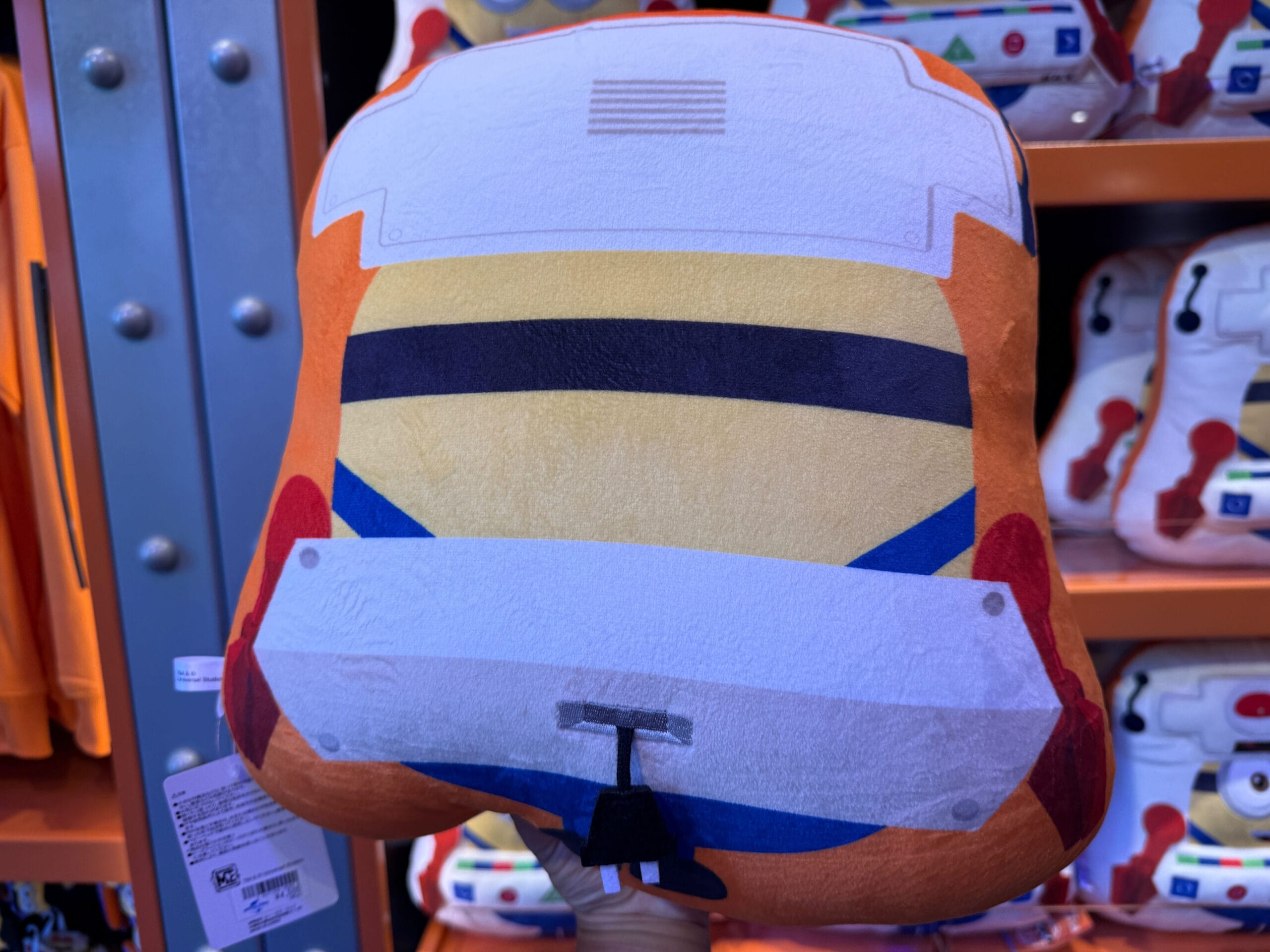 A plush pillow shaped like the back of a cartoon race car, displayed in a store with similar items in the background.