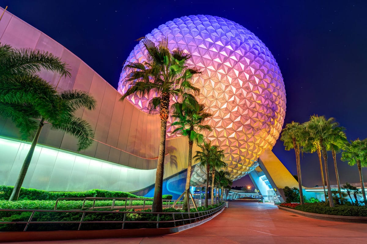 EPCOT’s Spaceship Earth geodesic sphere at night glows with color, showcasing Walt Disney World magic amid palm trees.