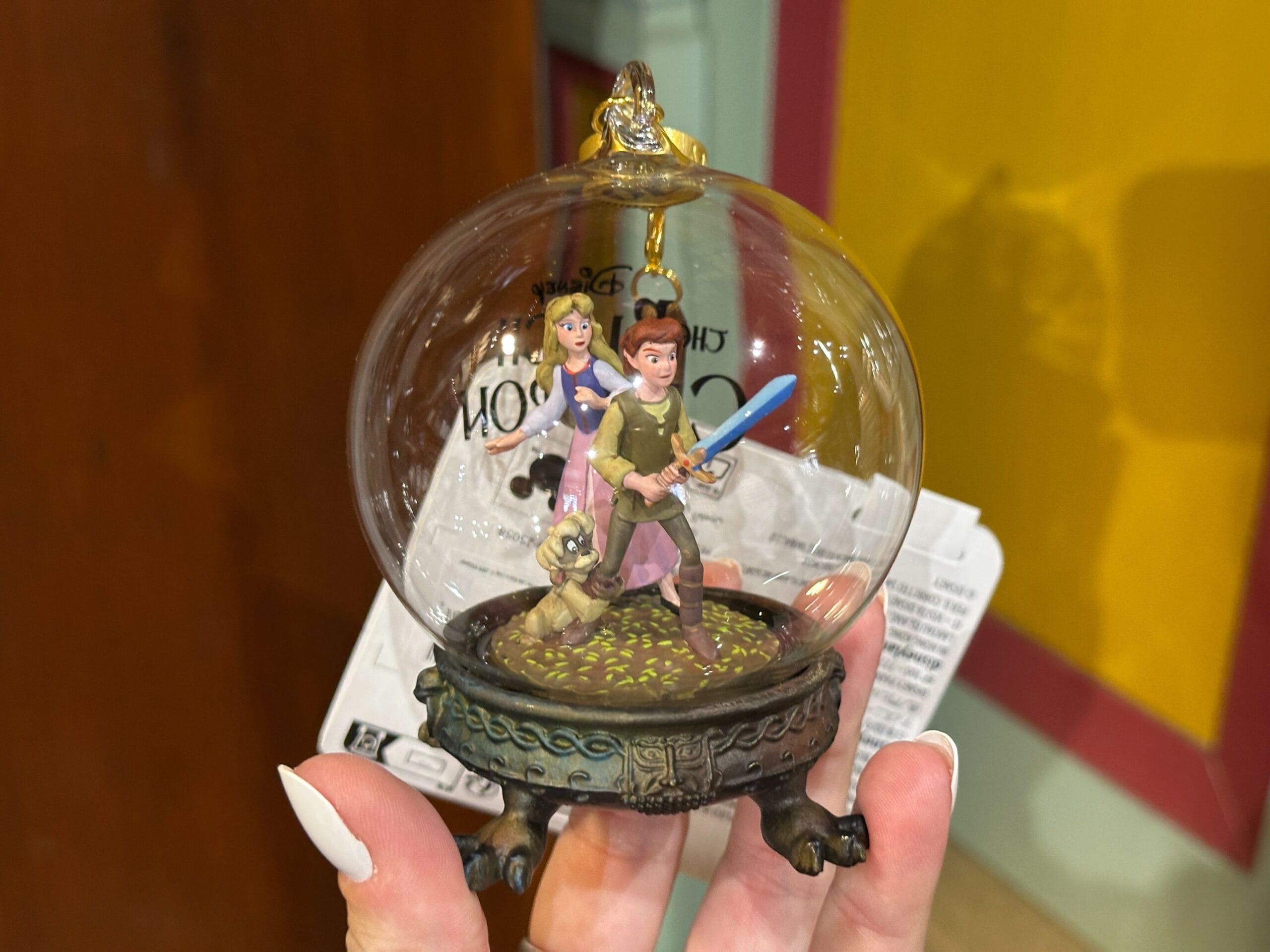 A hand holds a glass ornament featuring two animated characters and a small dog inside, standing ready for adventure.