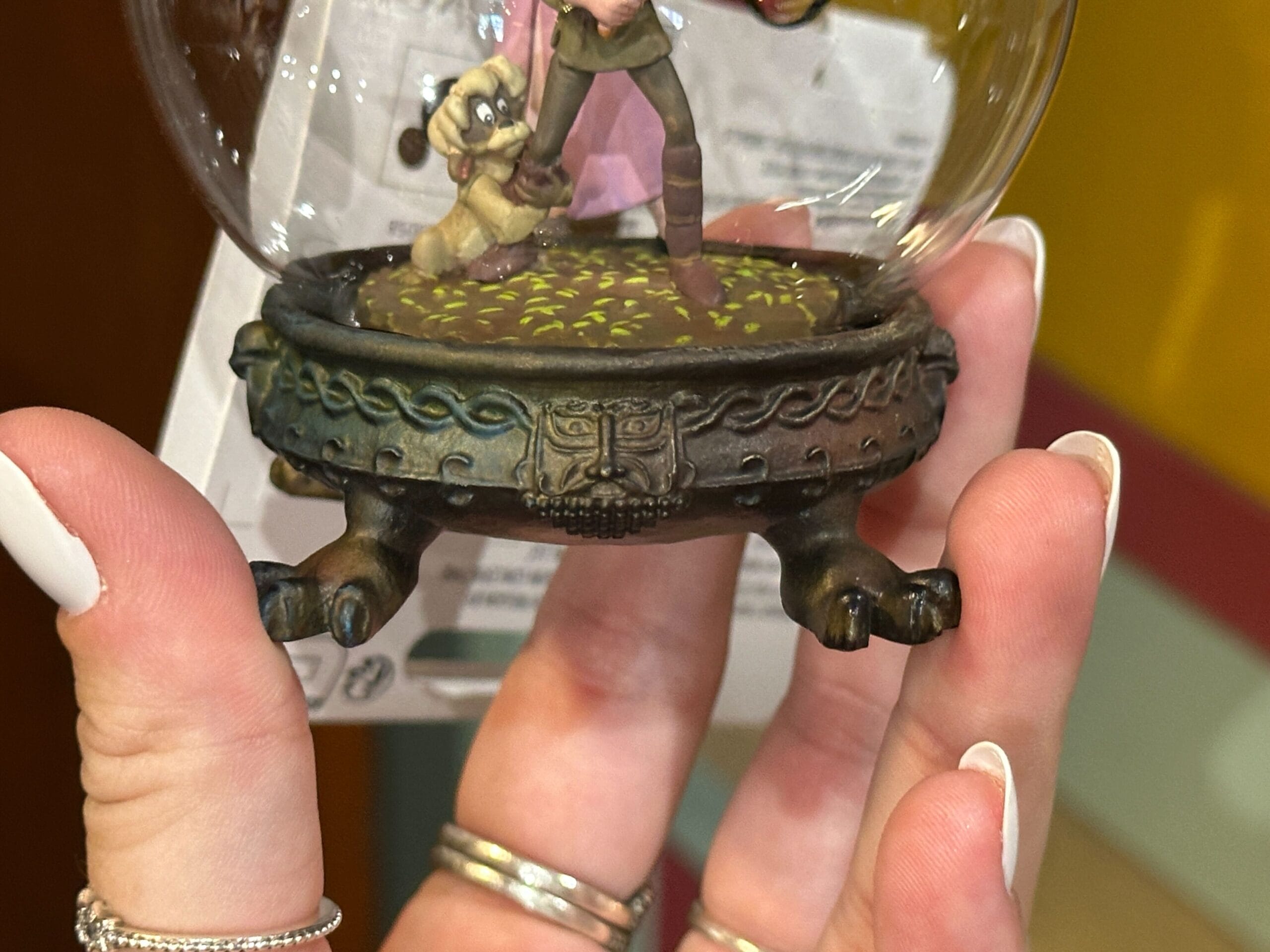 A hand holds a decorative globe with a detailed, ornate base featuring a carved face design and clawed feet.