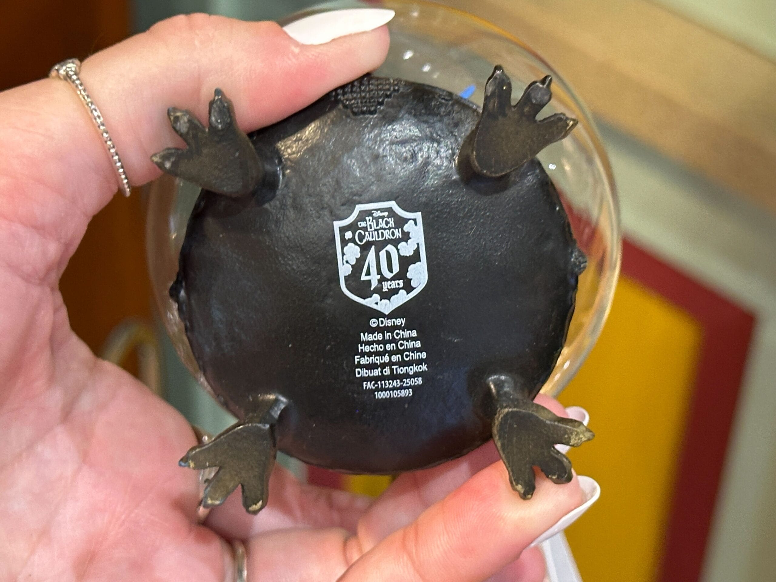 A hand holds a figurine base labeled "The Black Cauldron 40 Years" with four small animal feet.