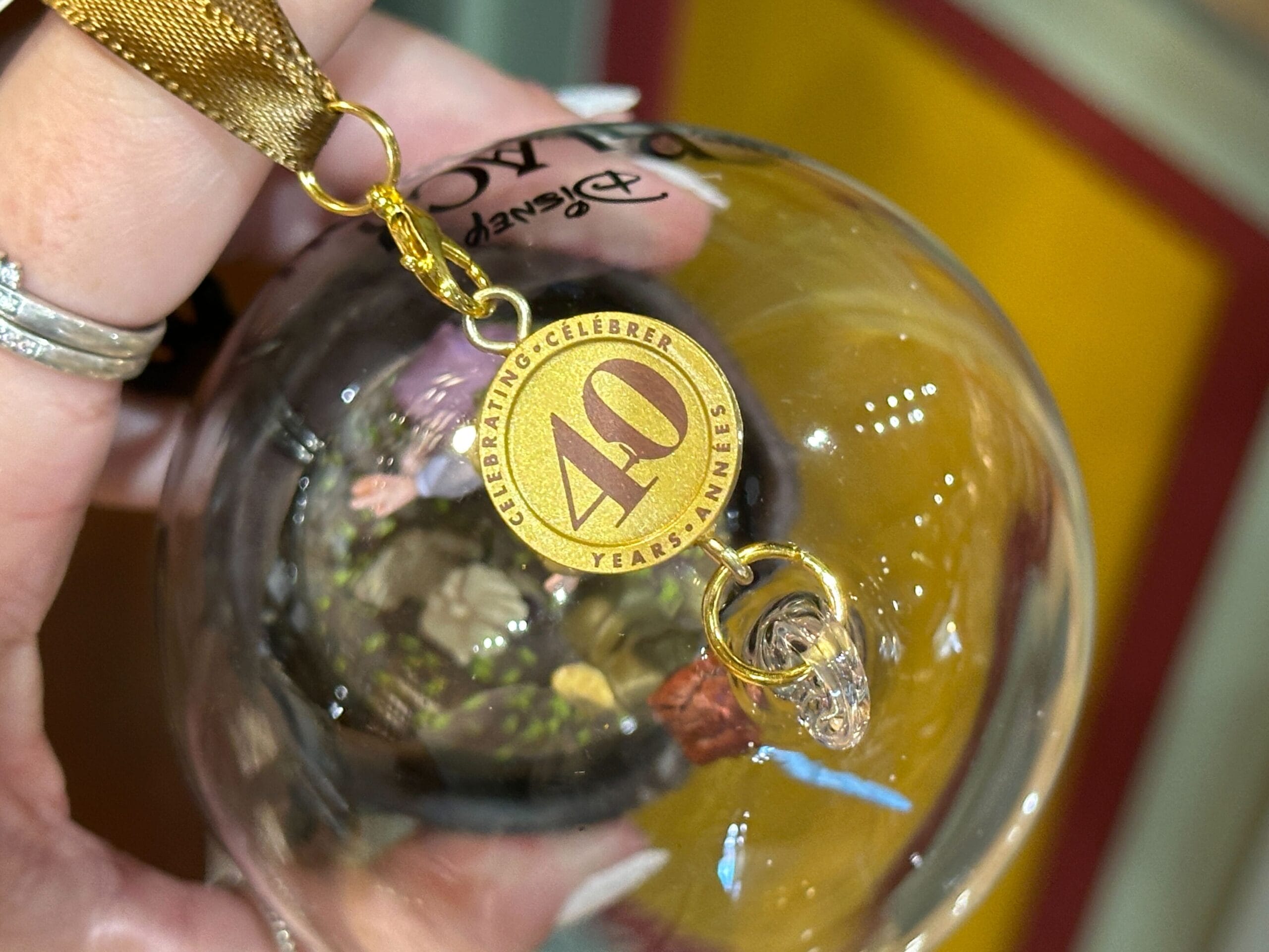 A hand holds a glass ornament with a gold "40 Years" celebratory charm attached by a ribbon.