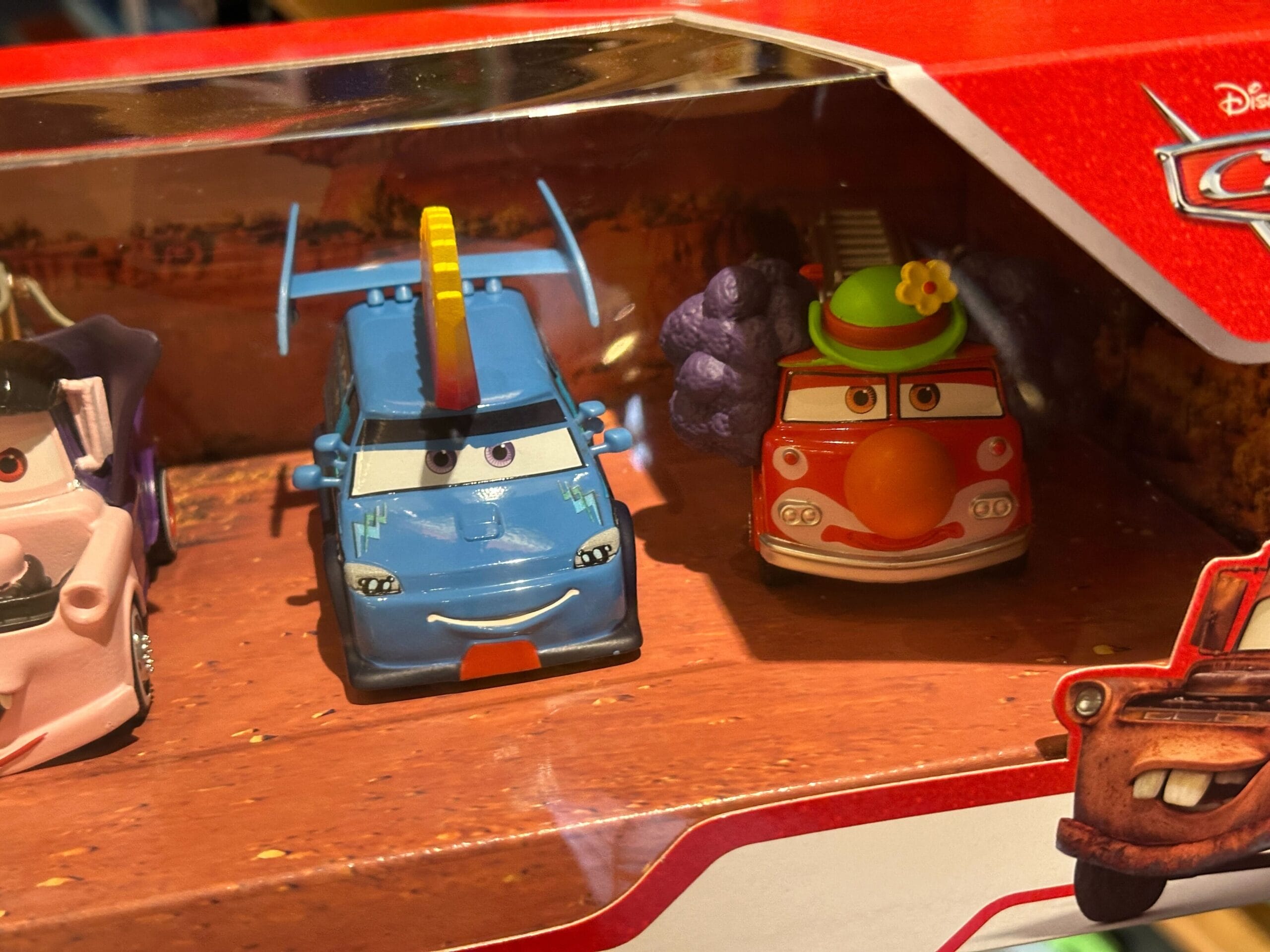 Two toy cars from Disney's Cars, DJ in blue with a mohawk and Red with a clown face, in a display box.
