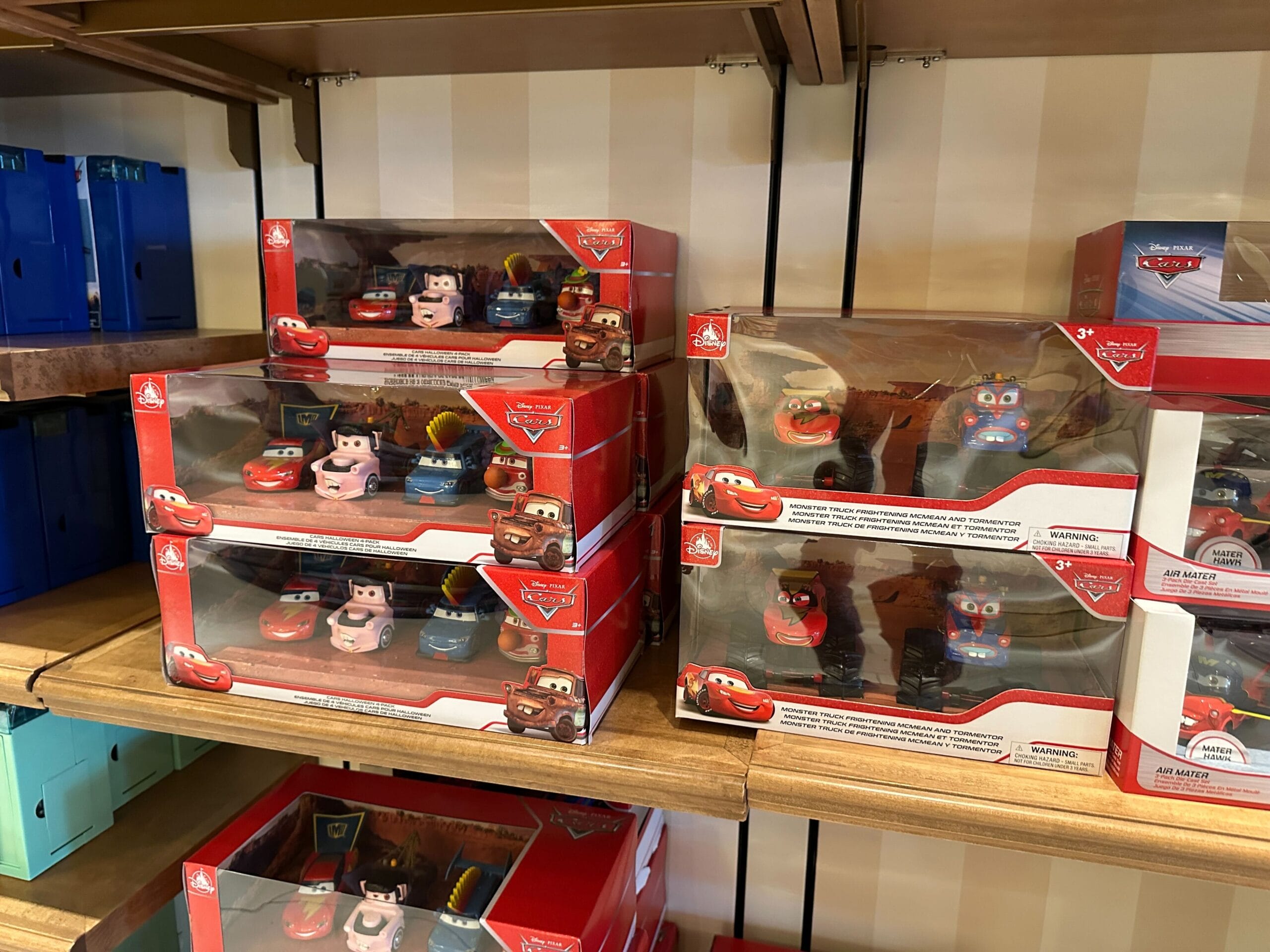 Toy Cars movie character sets in red packaging displayed on wooden store shelves.