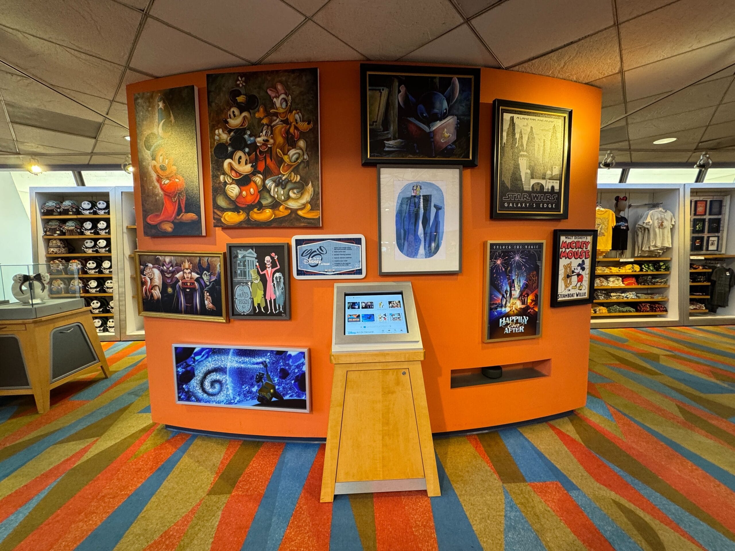 An orange wall displays Disney-themed art, a costume, and posters; a touchscreen kiosk stands in front.