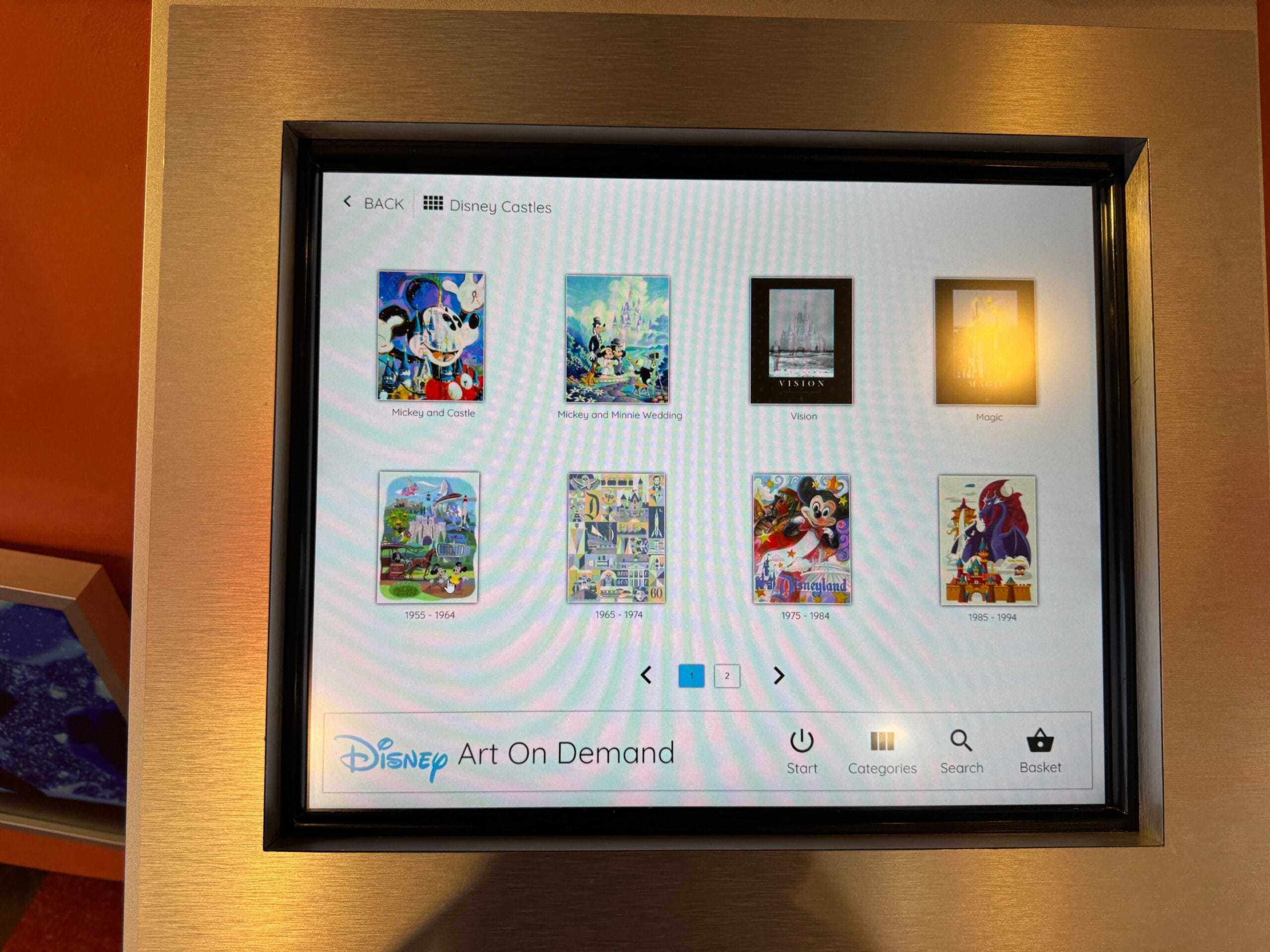 A touchscreen displays Disney art prints, including images of Mickey Mouse and various castles, with menu options below.