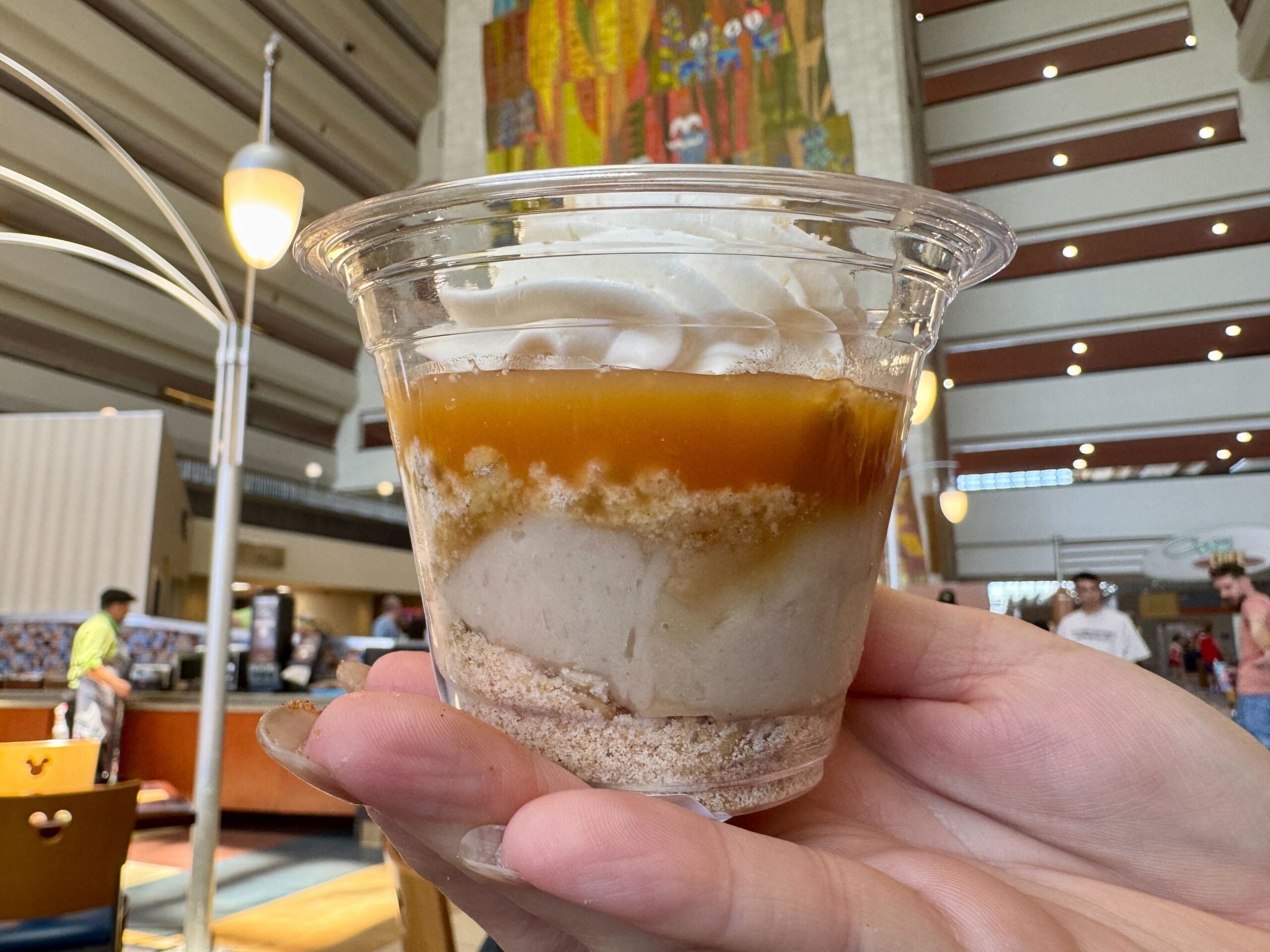 A hand holds a dessert cup layered with cream and caramel in the bright Contempo Cafe atrium, known for its desserts.