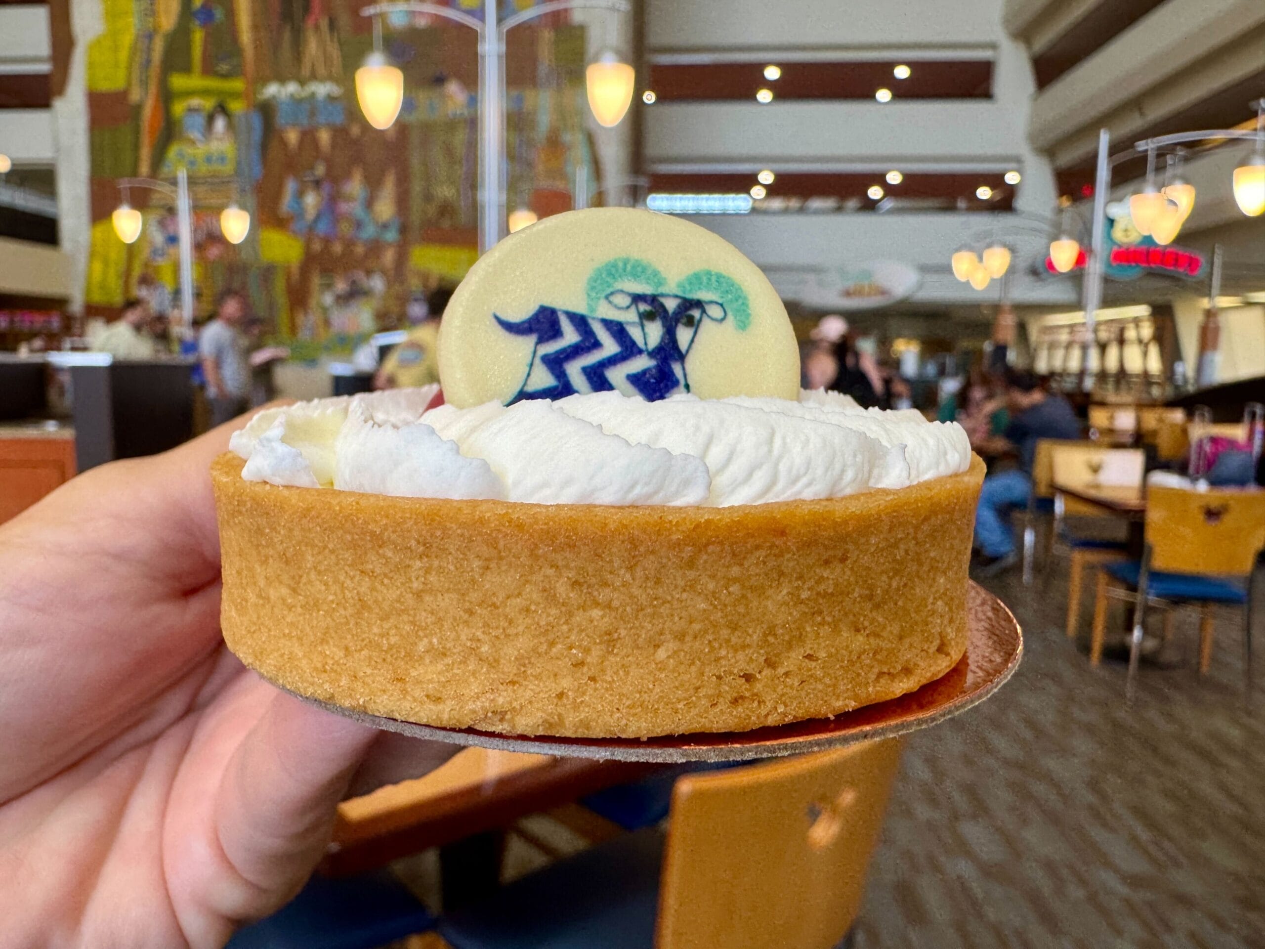 A hand holds a Contempo Cafe breakfast pastry topped with whipped cream and white chocolate in a bustling café.