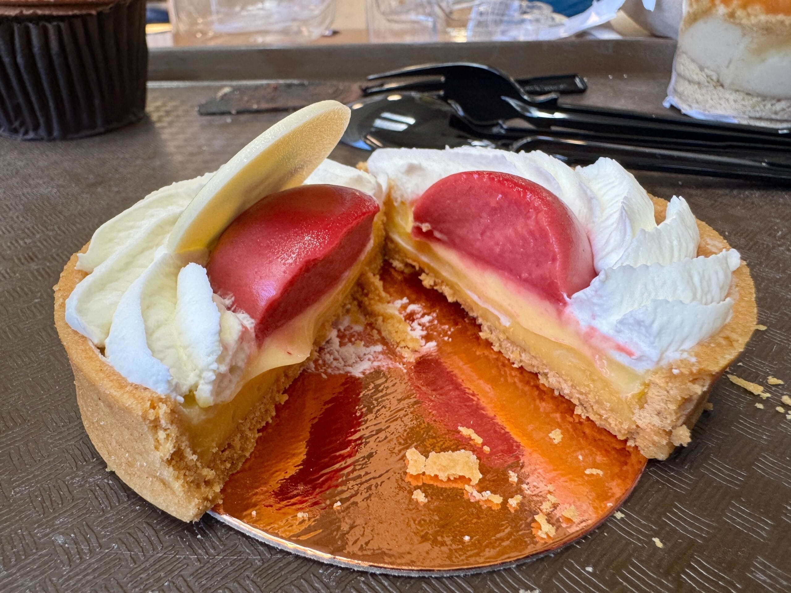 A sliced tart with cream and red fruit topping at Contempo Cafe, next to breakfast pastries and a chocolate muffin.